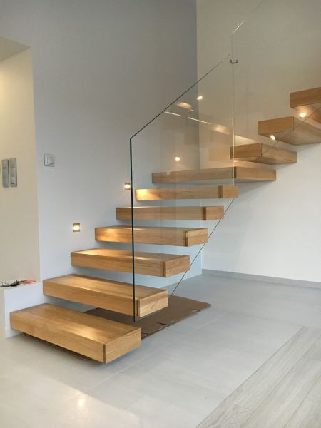 Nowoczesne schody wspornikowe z jasnego drewna z podświetleniem LED i szklaną balustradą, widok z dołu, częściowo zabezpieczone kartonem