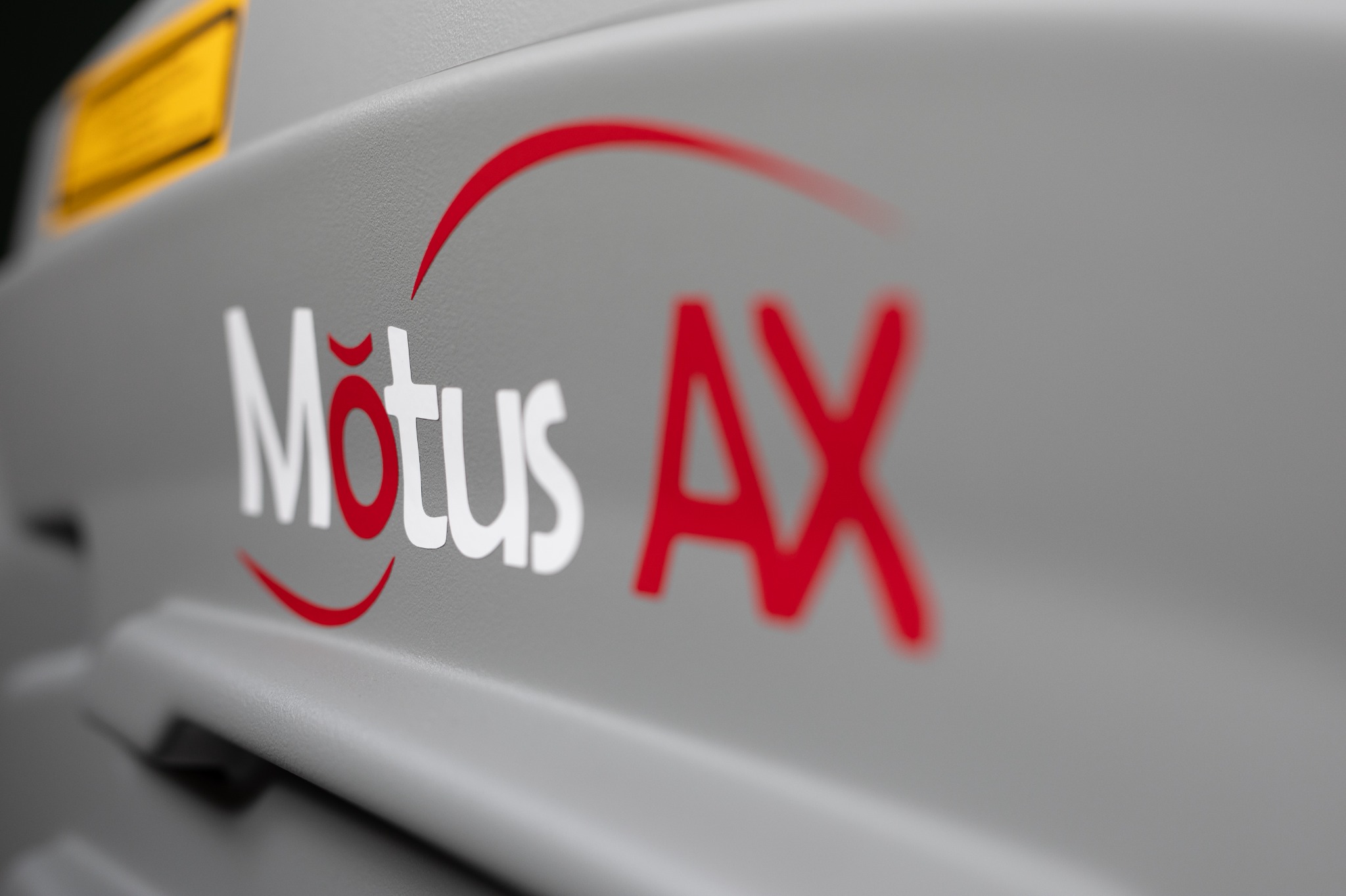 Szare urządzenie z białym napisem 'Motus' i czerwonym 'AX' oraz elementami graficznymi w tych samych kolorach, widoczne pod kątem.