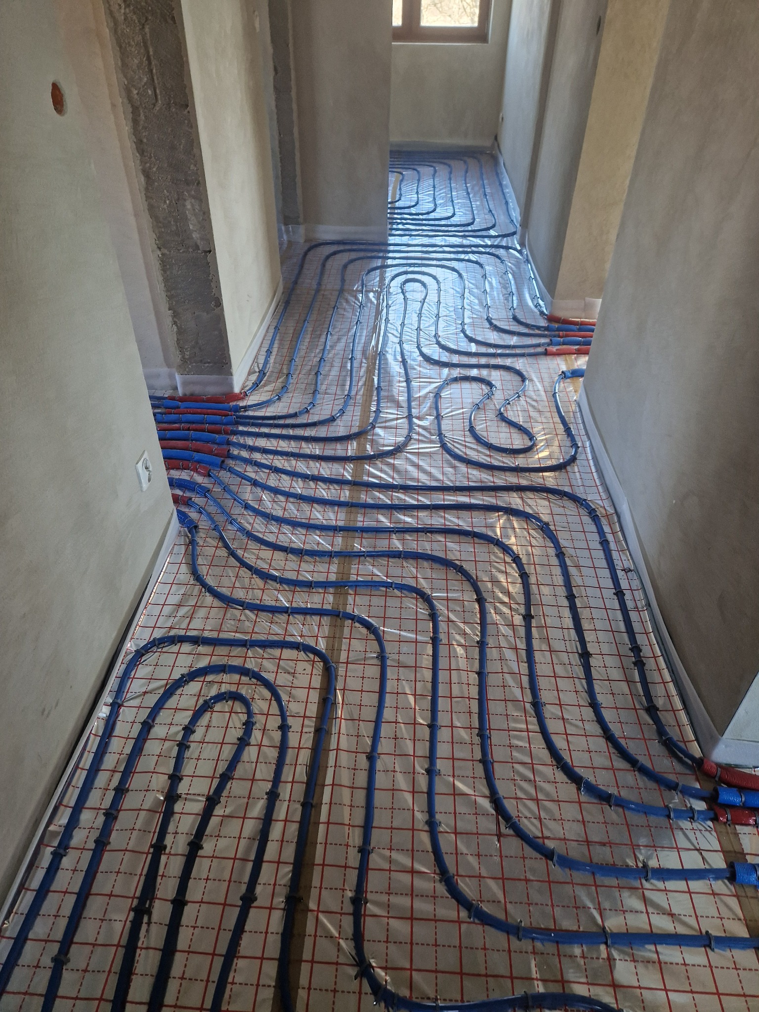 Montaż ogrzewania podłogowego w trakcie realizacji w Żywcu, widoczne nieotynkowane ściany i rury grzewcze ułożone na folii z siatką.