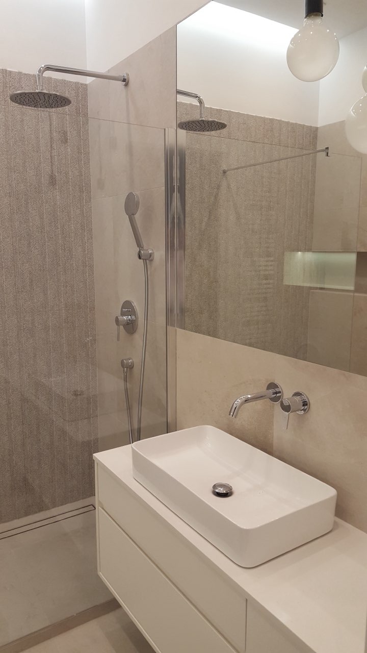 Nowoczesna łazienka z kabiną prysznicową typu walk-in, deszczownicą, umywalką nablatową na białej szafce i minimalistyczną armaturą w odcieniach srebra.