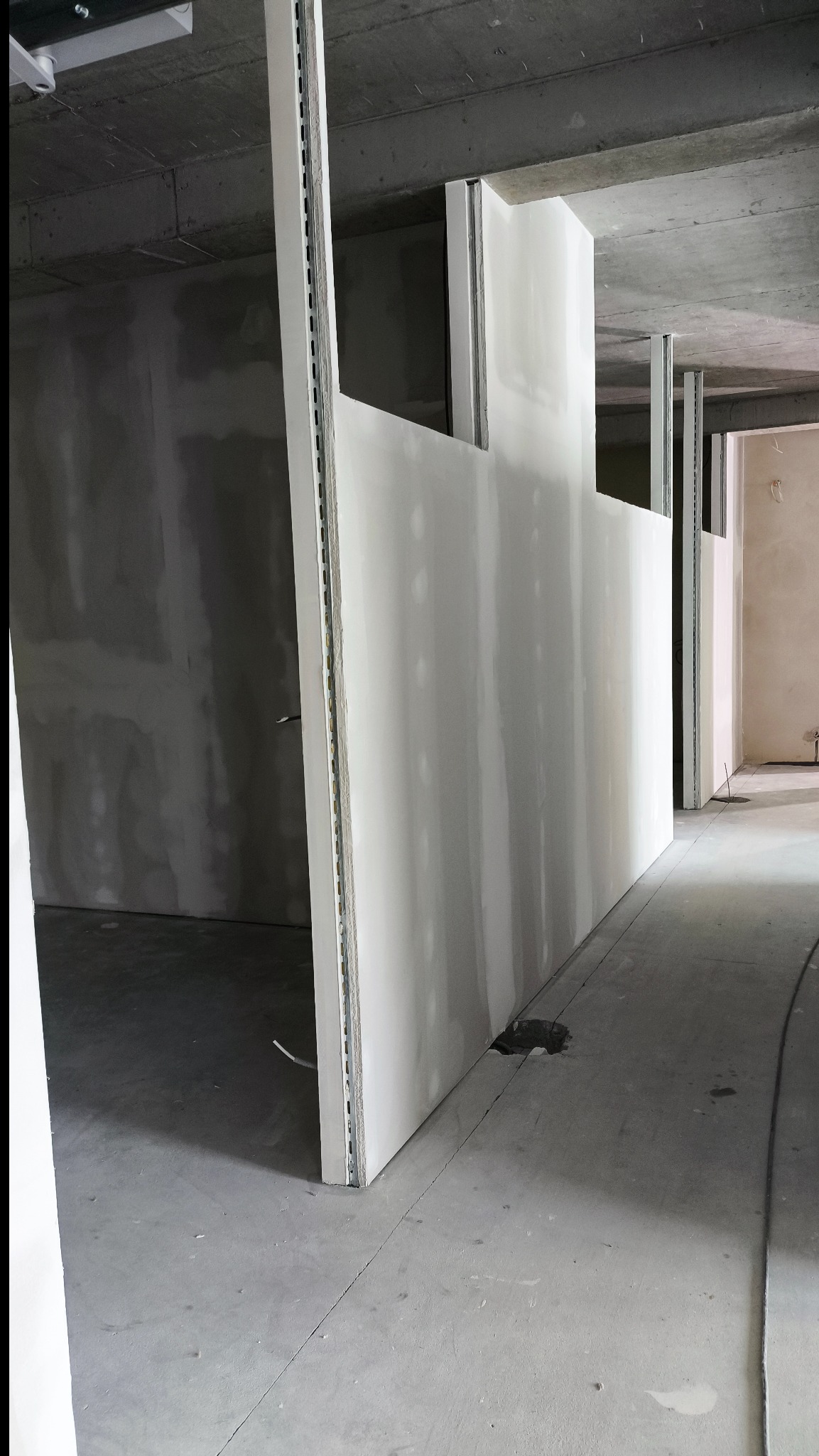 Montaż ścian działowych z płyt karton-gips na metalowym stelażu. Widoczne profile i surowy betonowy strop. W tle ściana po szpachlowaniu.