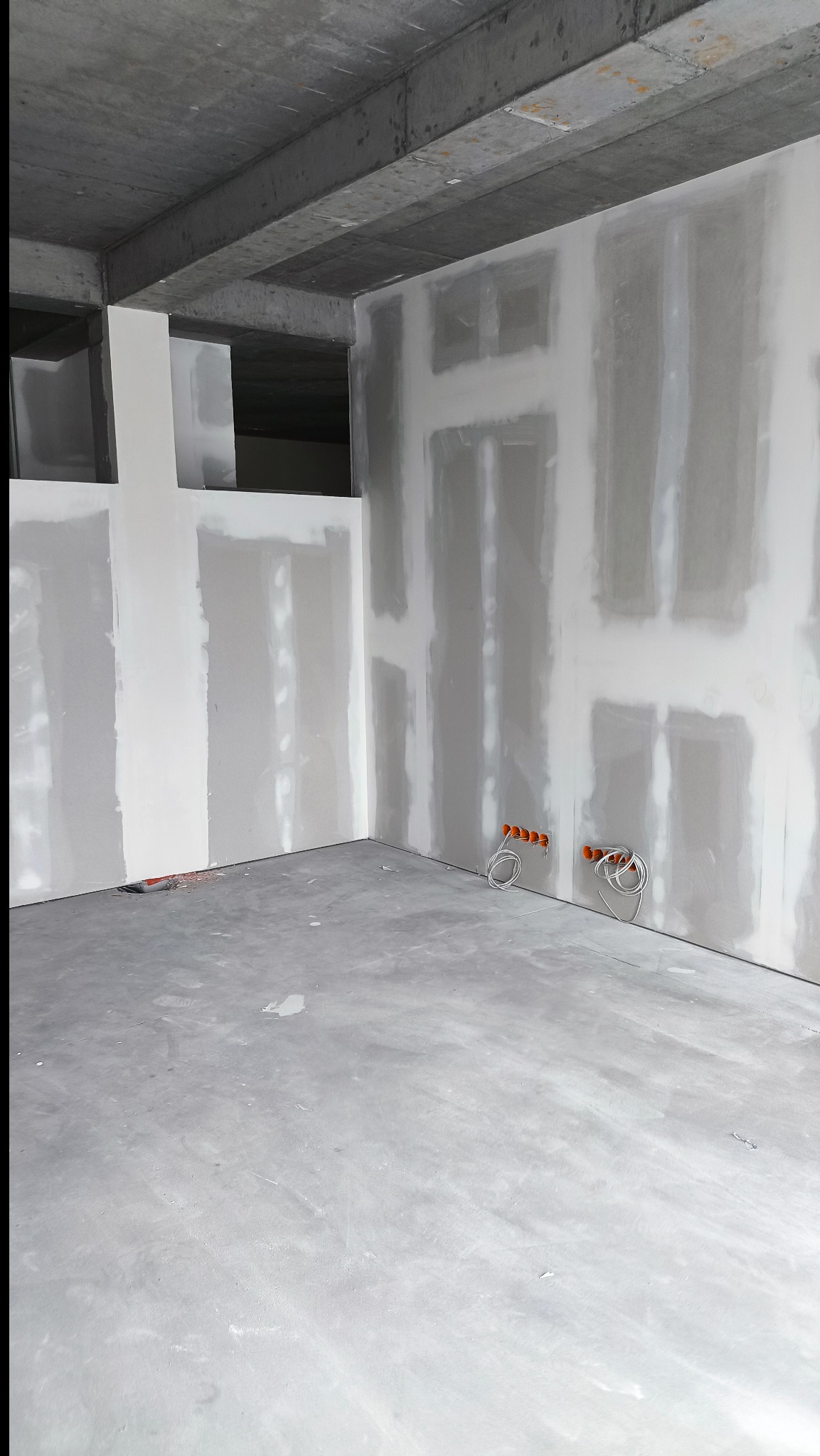 Surowe wnętrze w trakcie prac wykończeniowych: ściany z płyt karton-gips, widoczne puszki elektryczne, surowy betonowy strop. Minimalistyczny, industrialny charakter.