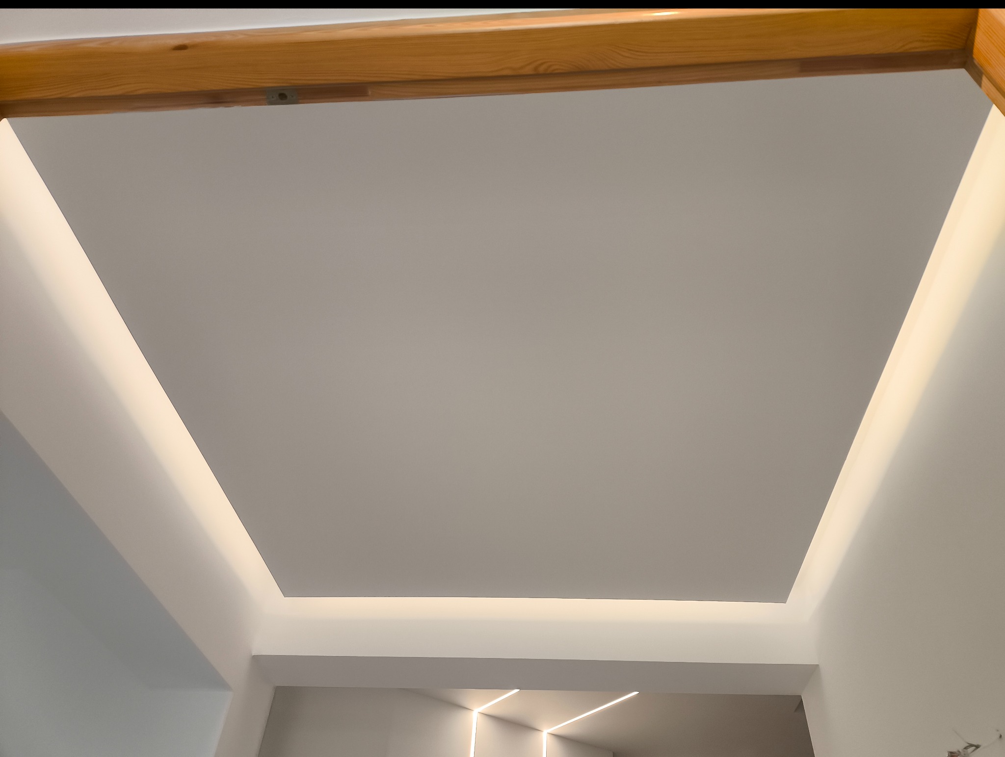 Podwieszany sufit z oświetleniem LED wzdłuż krawędzi, widok z dołu, drewniana rama w górnej części kadru. Minimalistyczny design, nowoczesne wykończenie wnętrza.