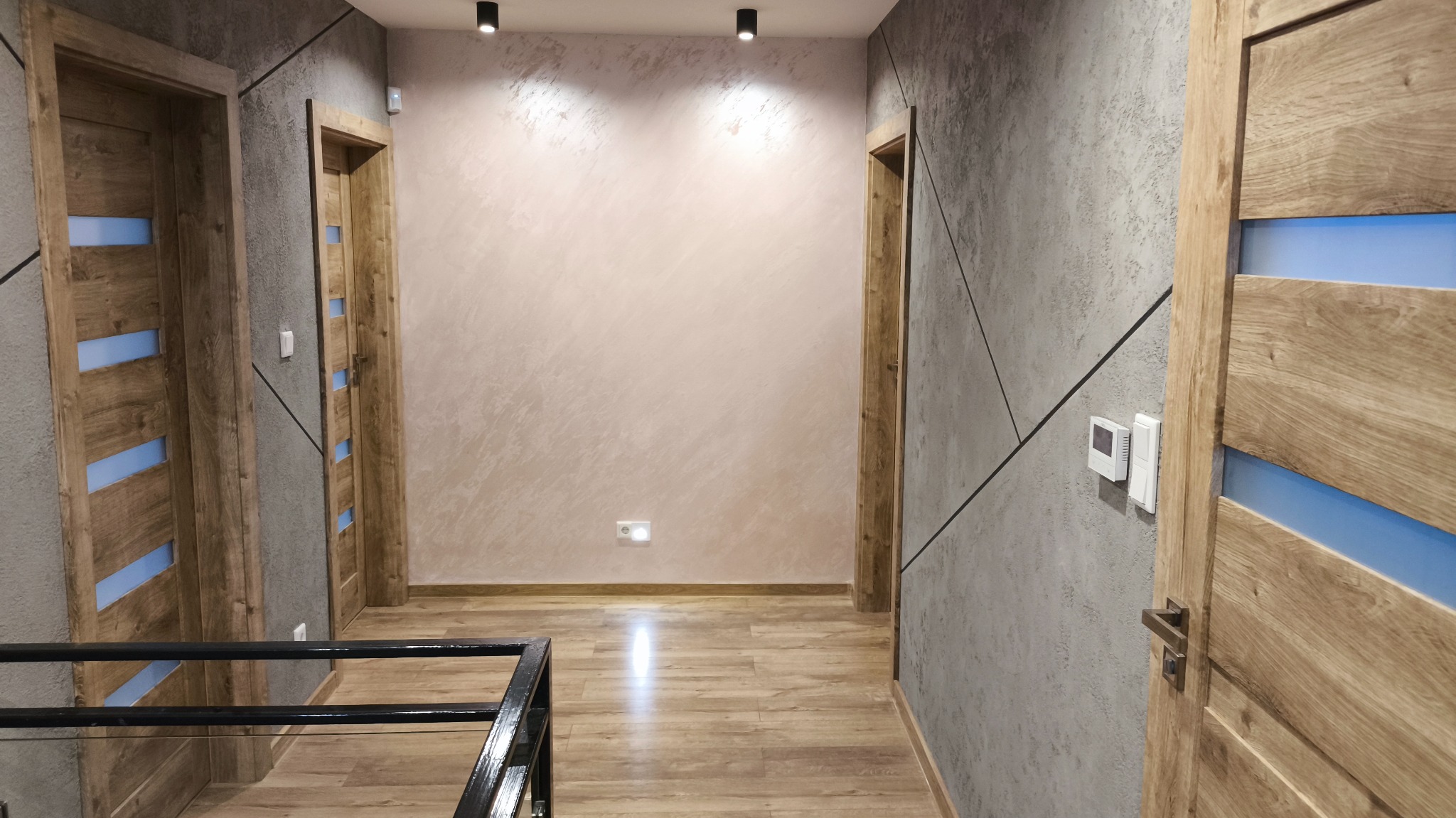 Nowoczesny korytarz po remoncie: szare ściany z geometrycznym wzorem, drewniane drzwi z niebieskimi akcentami, parkiet i oświetlenie punktowe. Widok z góry.