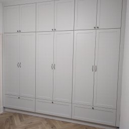 AWANGARDE - Jasnoszara, zabudowana szafa z górnymi szafkami i dolnymi szufladami, zamontowana na podłodze z parkietem w jodełkę. Widoczne narzędzia, sugerujące świeży montaż.