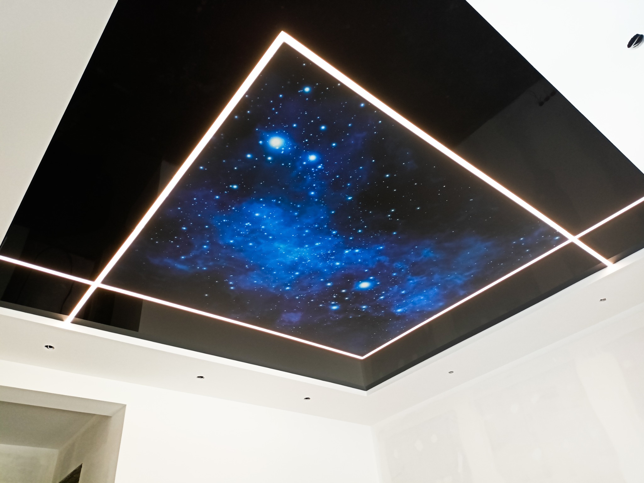 Czarny, błyszczący sufit napinany z motywem kosmosu, oświetlony liniami LED tworzącymi geometryczny wzór.