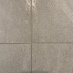 Szare, matowe płytki ceramiczne ułożone w kwadrat, z widocznymi fugami, delikatne odbicie światła na jednej z płytek.