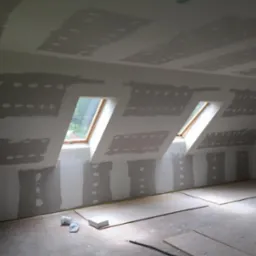 Poddasze w trakcie szpachlowania, widoczne okna dachowe, fragmenty płyt kartonowo-gipsowych na ścianach i suficie, szpachla na łączeniach, przygotowanie do dalszych prac wykończeniowych.