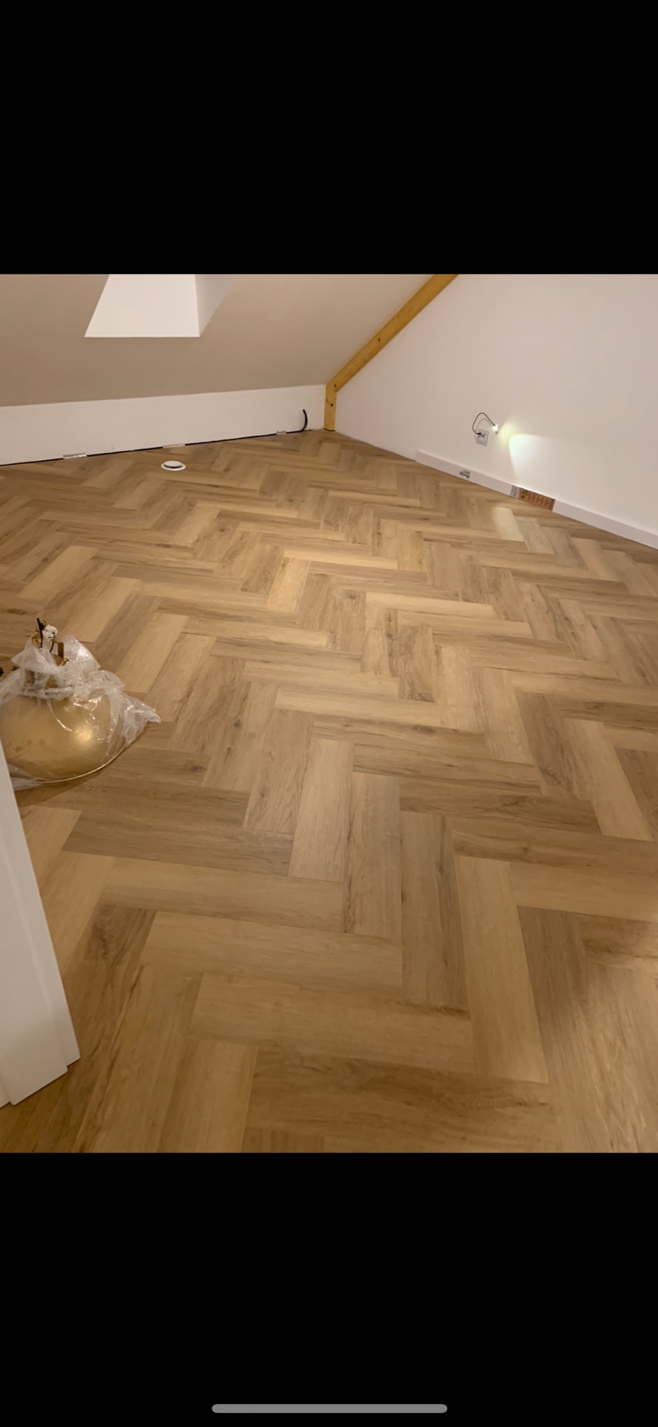 Ukończone podłogi z paneli ułożonych w jodełkę w pokoju na poddaszu, widoczne listwy przypodłogowe i wystający kabel elektryczny.