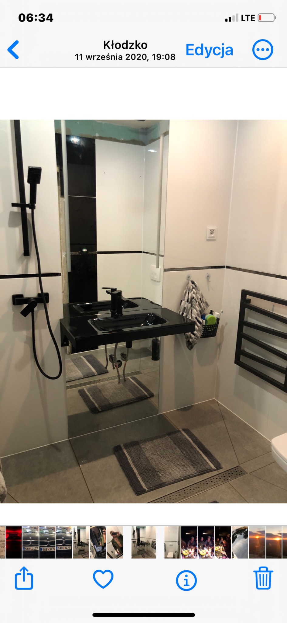 Nowoczesna łazienka z czarną armaturą, umywalką na lustrzanej półce, grzejnikiem drabinkowym i szarą wycieraczką na podłodze z odpływem liniowym.