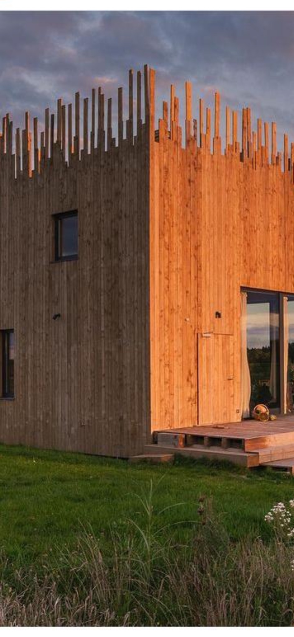 Nowoczesna elewacja budynku z drewnianymi elementami w Jaszkówce, widoczna z zewnątrz, z unikalnym pionowym układem desek na szczycie i ciepłym oświetleniem słonecznym.