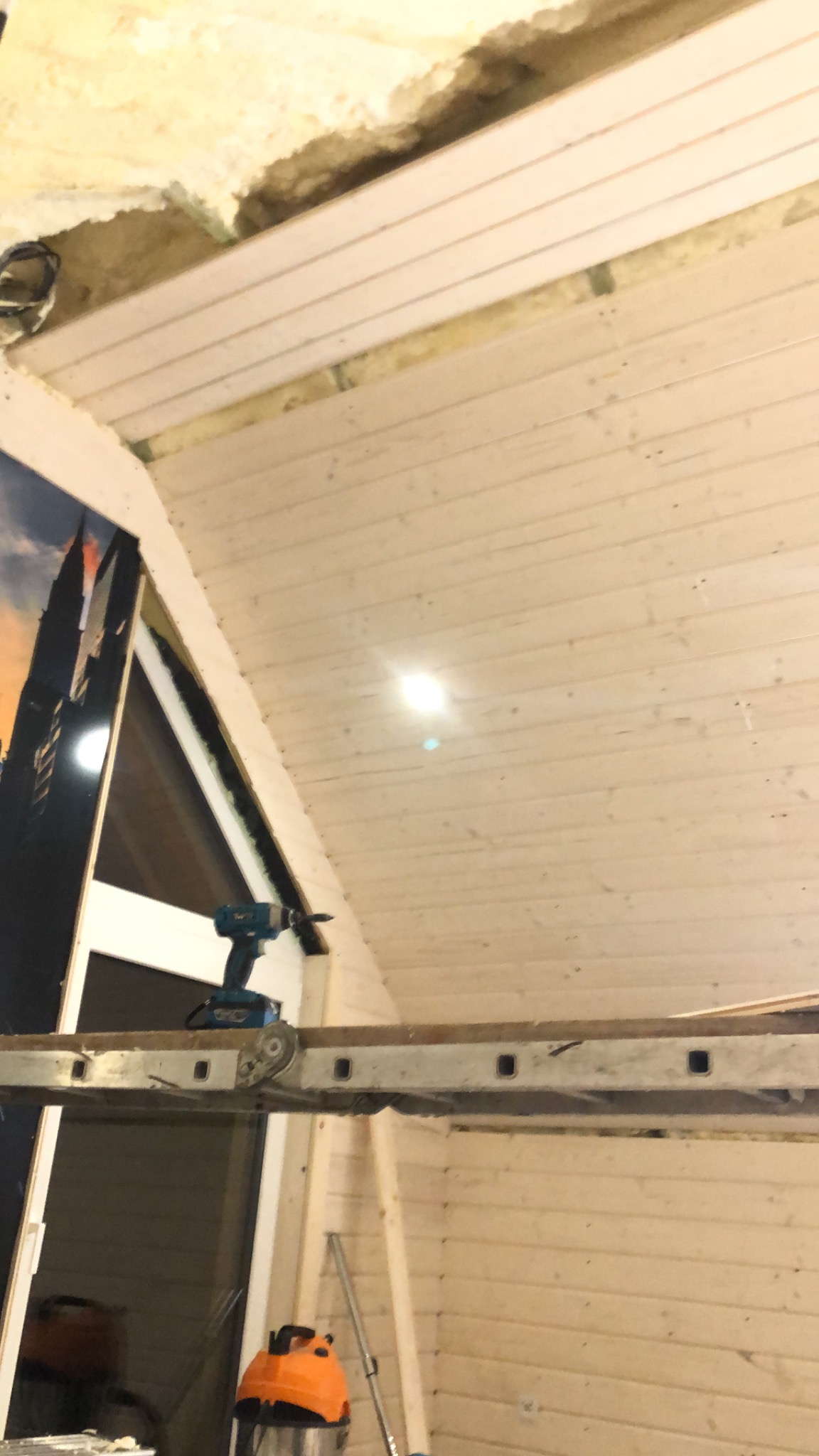 Drewniana boazeria na skośnym suficie poddasza, widoczna drabina i wkrętarka akumulatorowa podczas montażu.