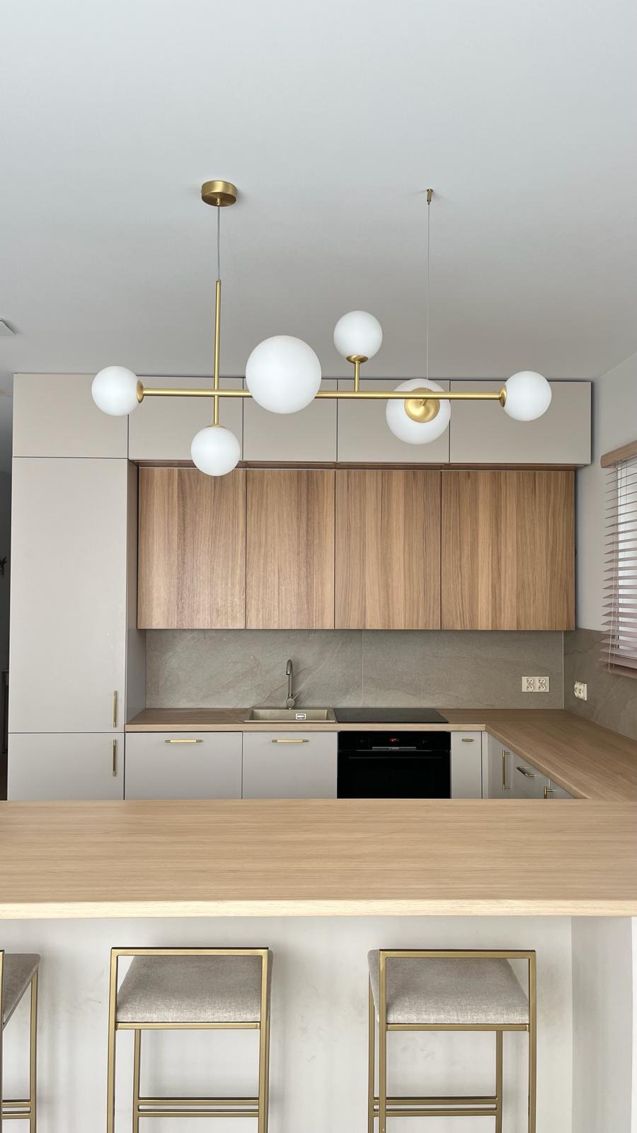 Nowoczesna kuchnia z drewnianymi frontami szafek górnych, szarymi szafkami dolnymi, blatem z jasnego drewna i złotą lampą z kulistymi kloszami.