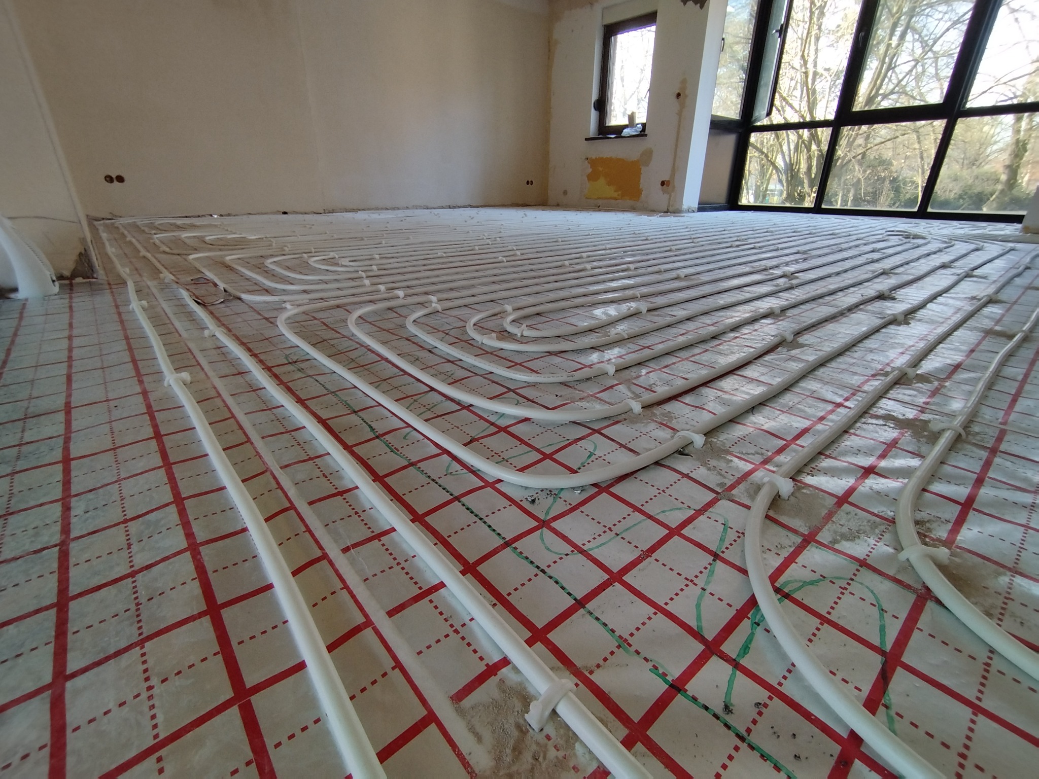 Białe rury ogrzewania podłogowego ułożone na folii z czerwoną kratką w pomieszczeniu w Namysłowie, przygotowane do zalania wylewką.