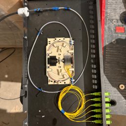 IT-One Sebastian Jasnoch - Panel światłowodowy z podłączonymi kablami światłowodowymi i złączami, widoczne narzędzia i akcesoria montażowe na stole roboczym.