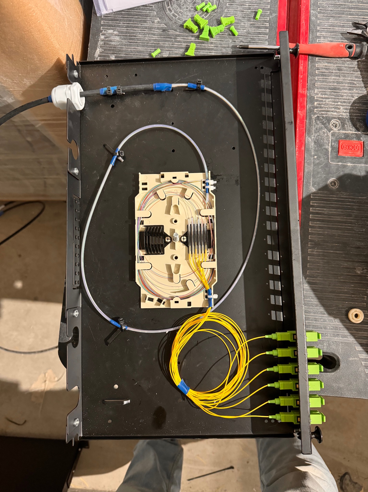 Panel światłowodowy z podłączonymi kablami światłowodowymi i złączami, widoczne narzędzia i akcesoria montażowe na stole roboczym.