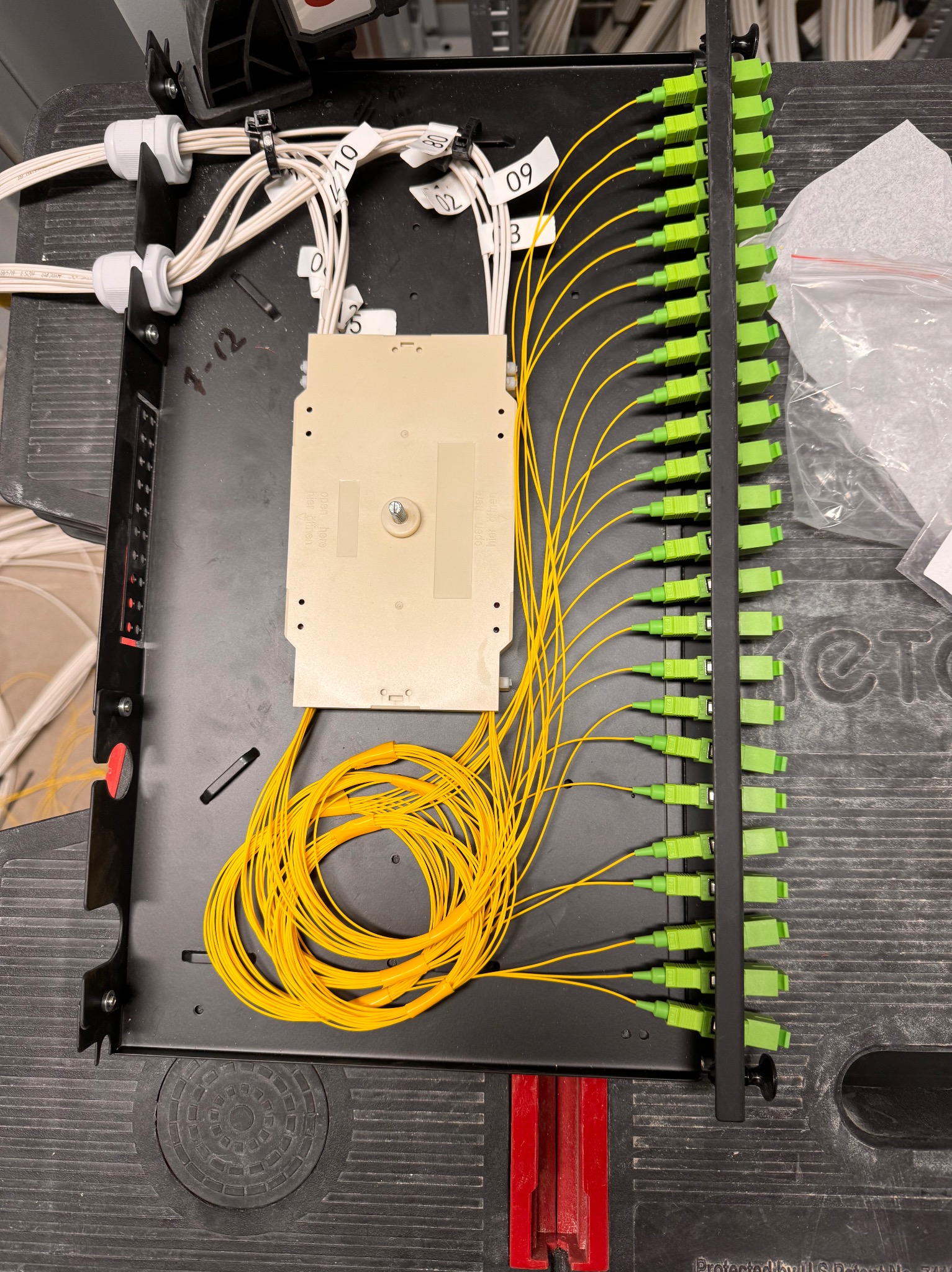 Panel krosowniczy z podłączonymi światłowodami oznaczonymi numerami, zwinięty zapas kabli na dnie skrzynki.