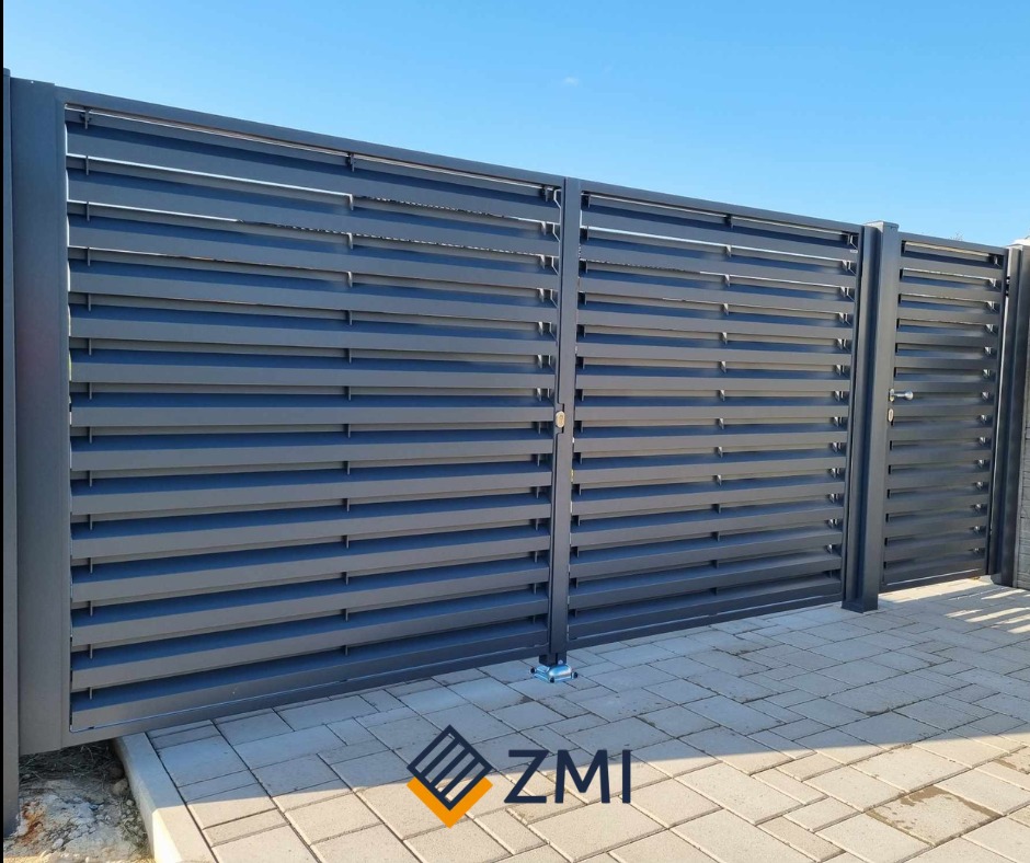 Nowoczesna, metalowa brama posesyjna z poziomymi lamelami w kolorze grafitowym, widoczna od strony podjazdu wyłożonego kostką brukową.