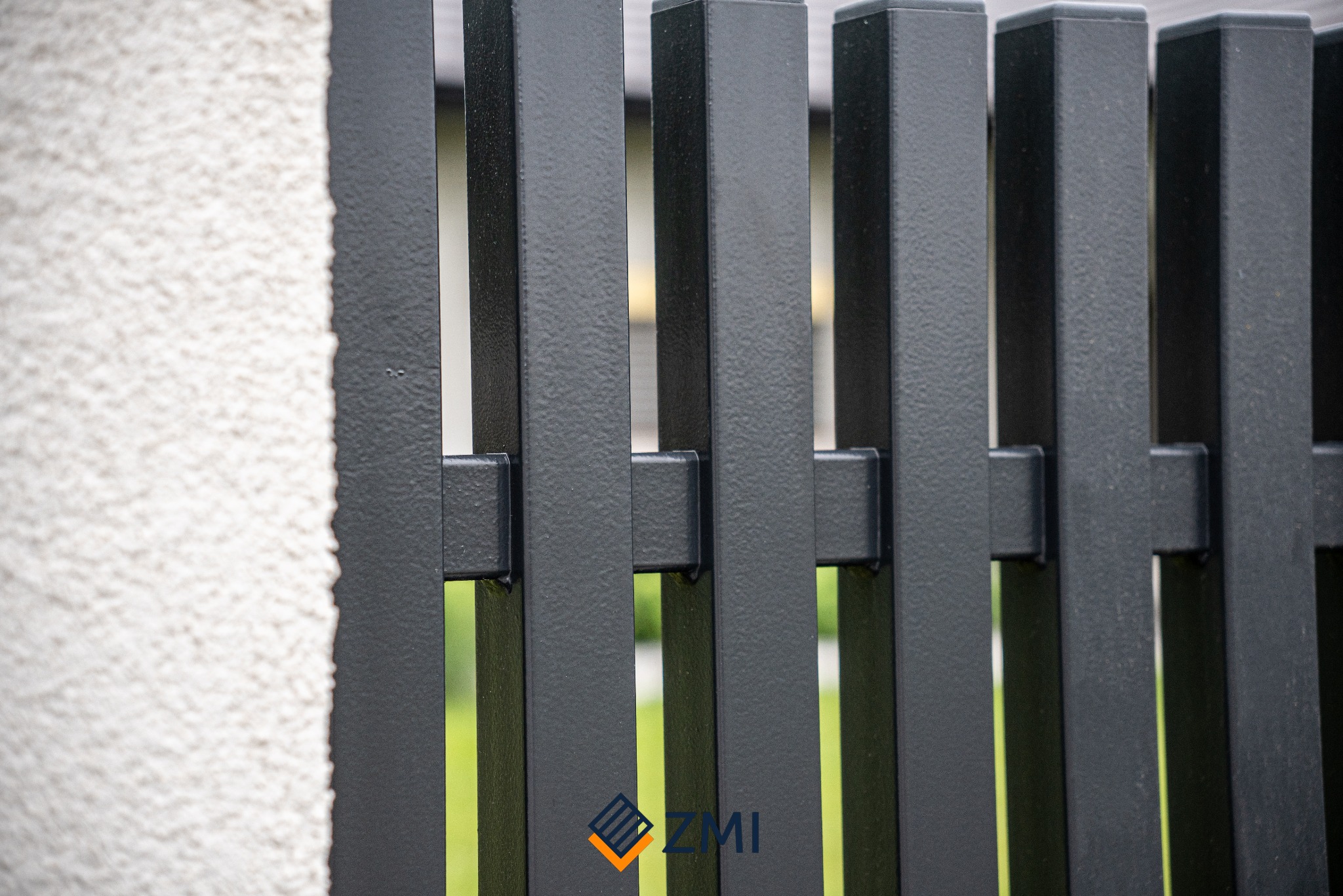 Fragment nowoczesnego, matowego, grafitowego ogrodzenia panelowego z bliska, widoczne elementy mocujące i struktura tynku na słupku obok.