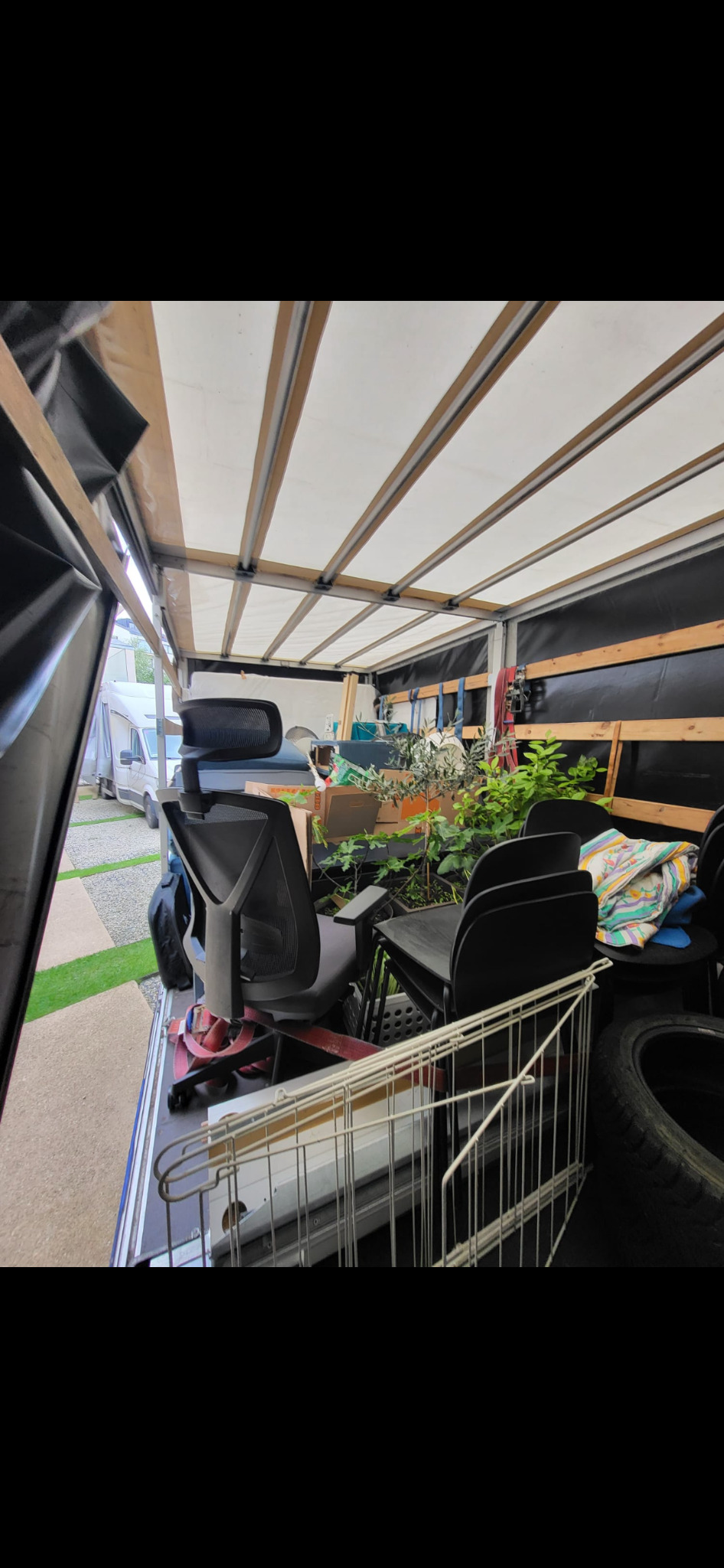 Wnętrze przestrzeni ładunkowej busa wypełnione meblami biurowymi, roślinami doniczkowymi i innymi przedmiotami podczas transportu.