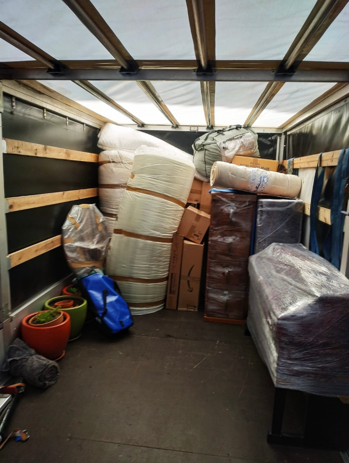 Wnętrze przestrzeni ładunkowej wypełnionej zabezpieczonymi meblami, kartonami i roślinami doniczkowymi podczas transportu.