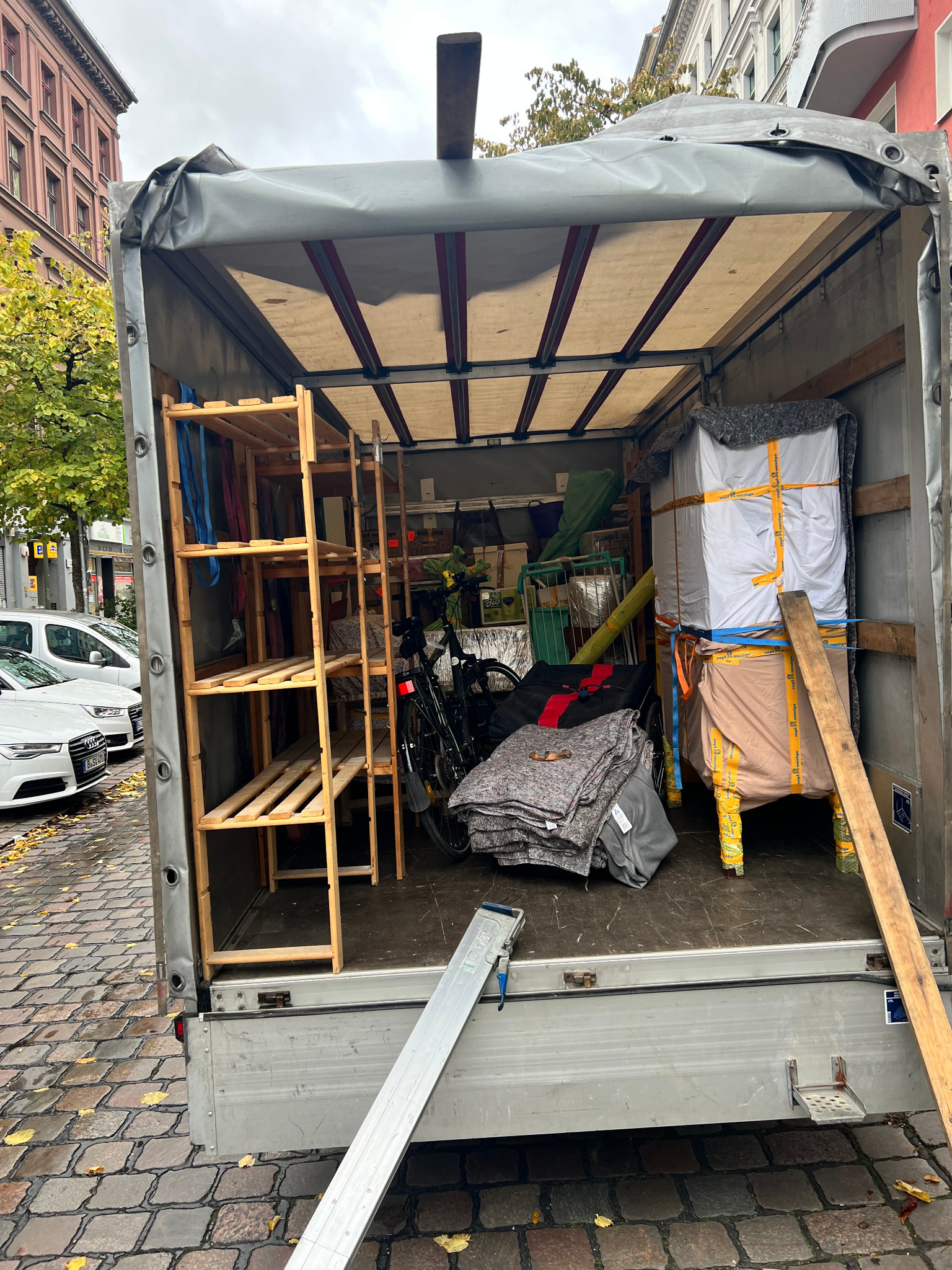 Wnętrze samochodu dostawczego wypełnione meblami, rowerem i zabezpieczonymi przedmiotami podczas transportu na brukowanej ulicy.