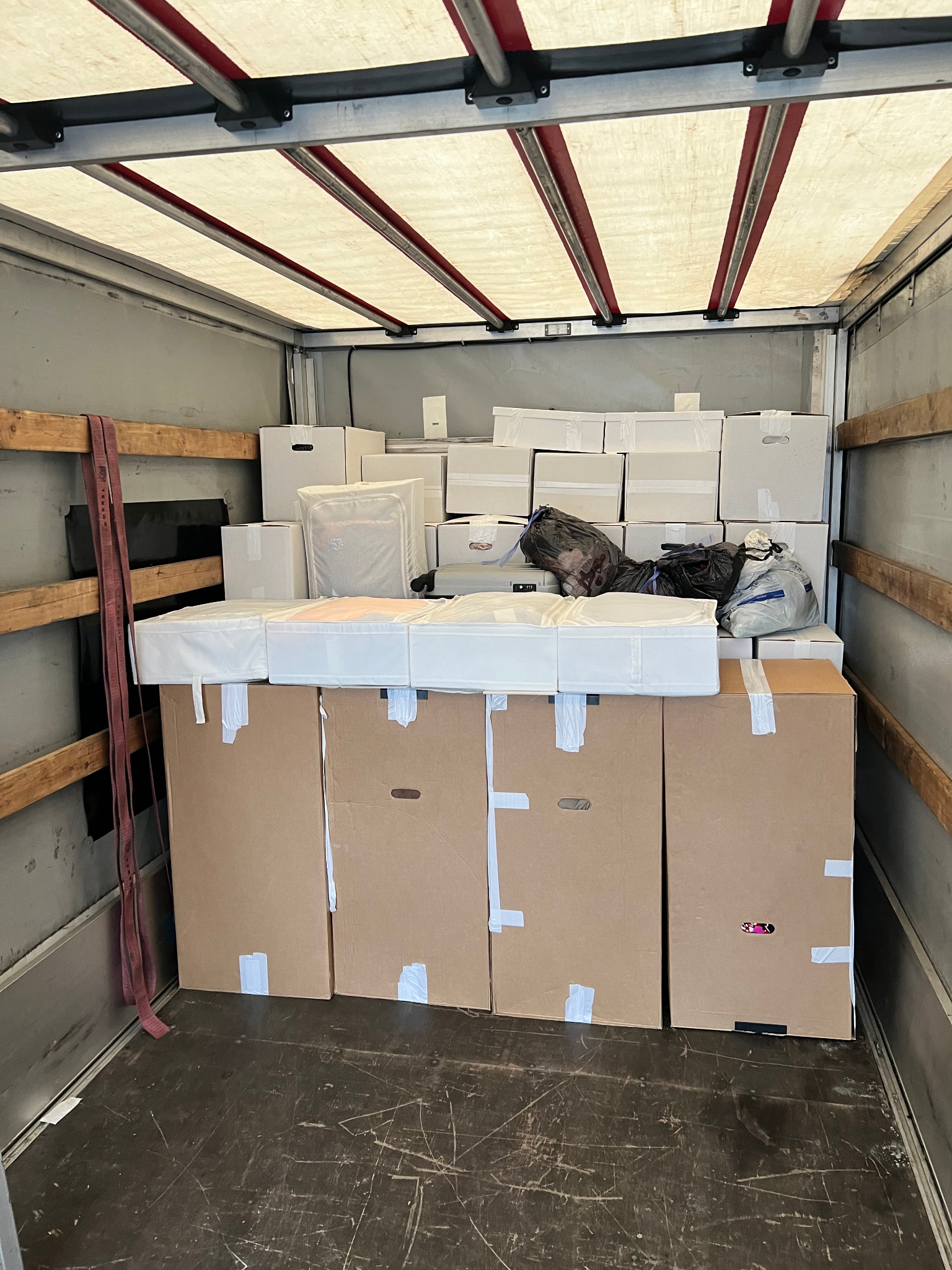 Wnętrze skrzyni ładunkowej wypełnione kartonami, białymi pudełkami i workami, zabezpieczonymi taśmą, gotowymi do transportu.