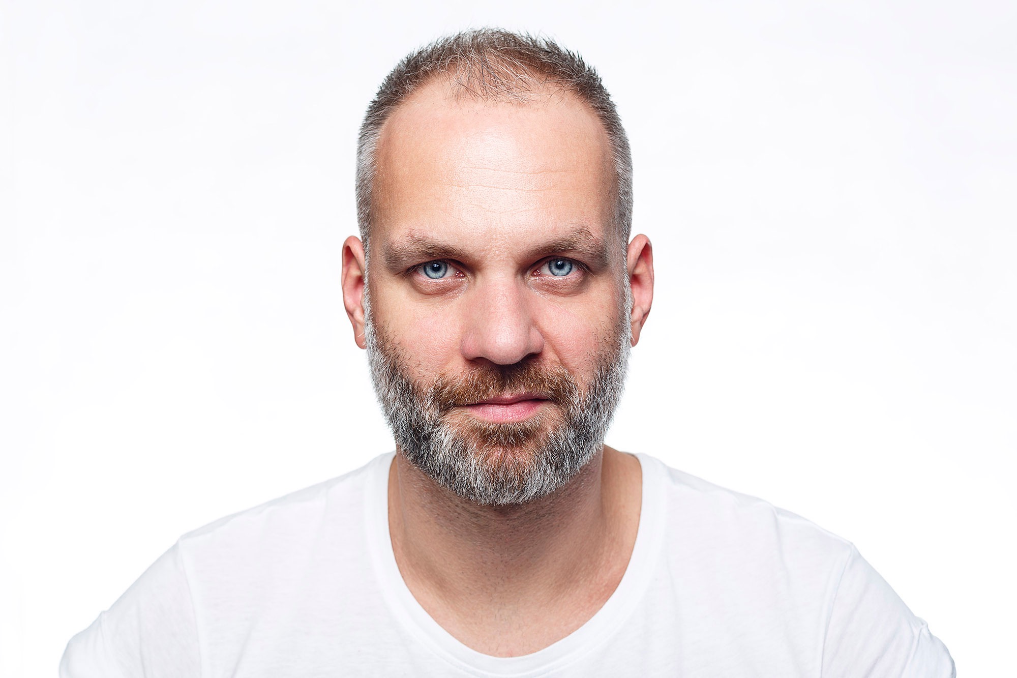 Portret mężczyzny z krótkimi włosami i brodą na białym tle, wyraźne niebieskie oczy.