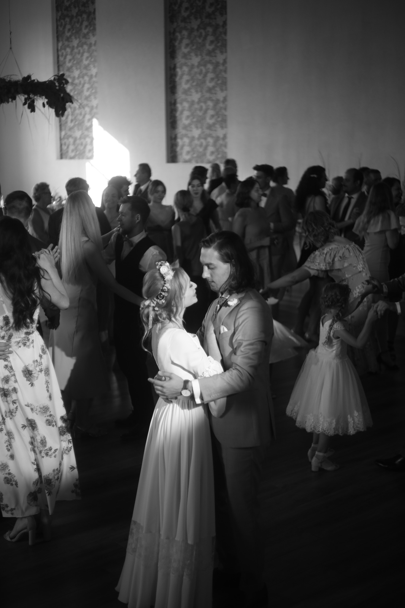 Czarno-białe zdjęcie pary młodej podczas pierwszego tańca na weselu, otoczonej przez gości.