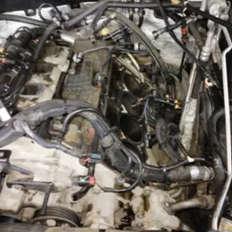 Widok z góry na otwarty silnik samochodowy z widocznymi cylindrami, przewodami i innymi elementami osprzętu w trakcie naprawy.