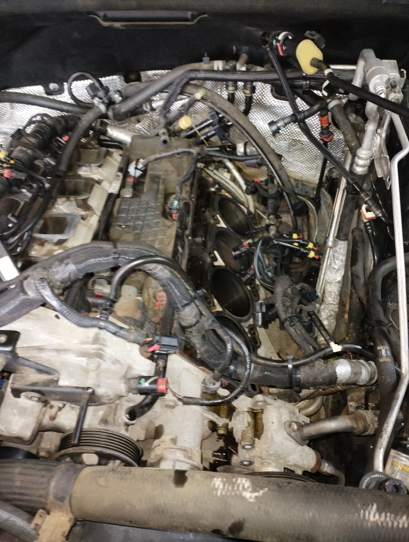 Widok z góry na otwarty silnik samochodowy z widocznymi cylindrami, przewodami i innymi elementami osprzętu w trakcie naprawy.