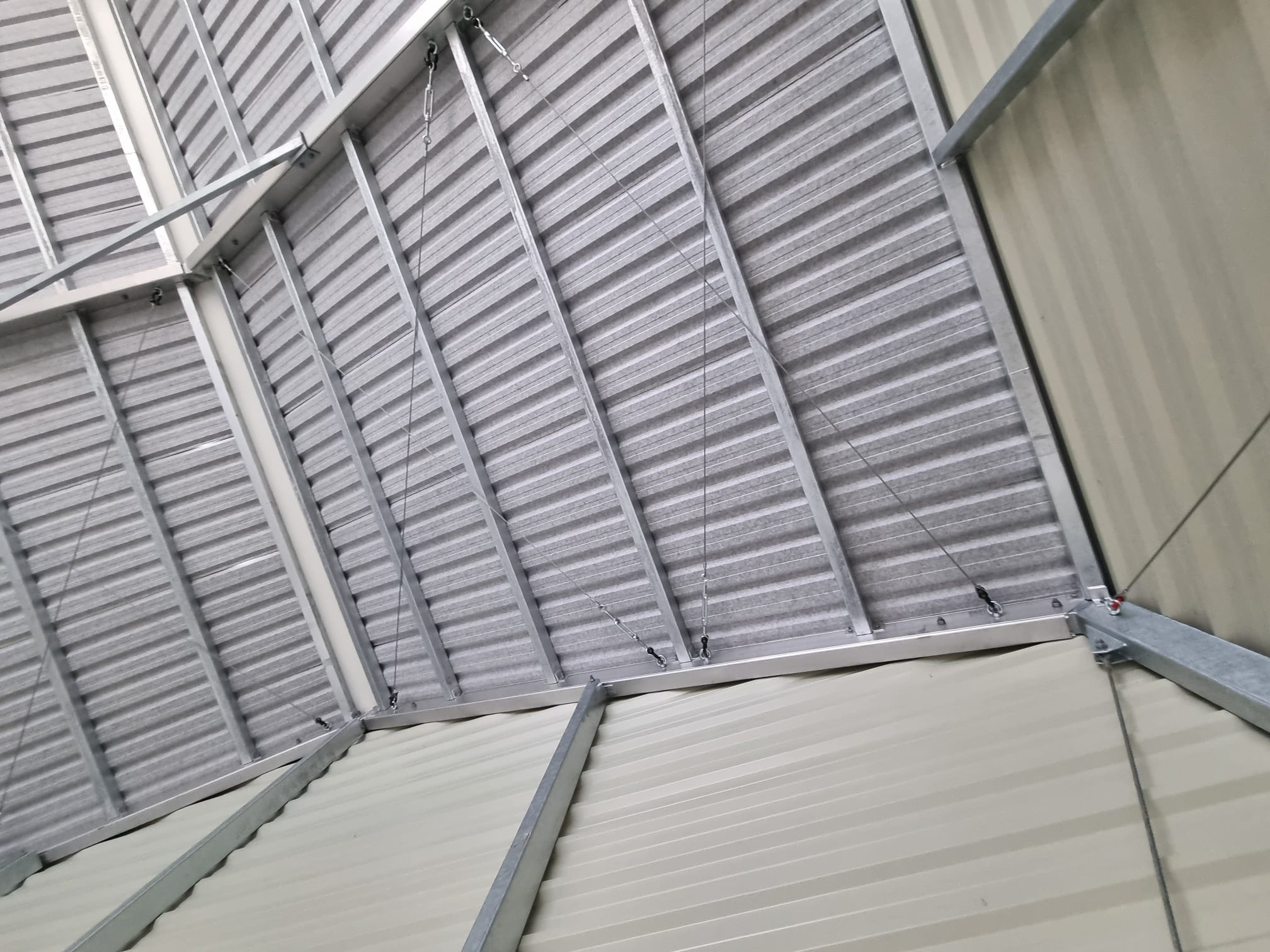Wnętrze hali w trakcie budowy, widoczne stalowe elementy konstrukcyjne i blacha trapezowa pod kątem, z detalami mocowań i linek.