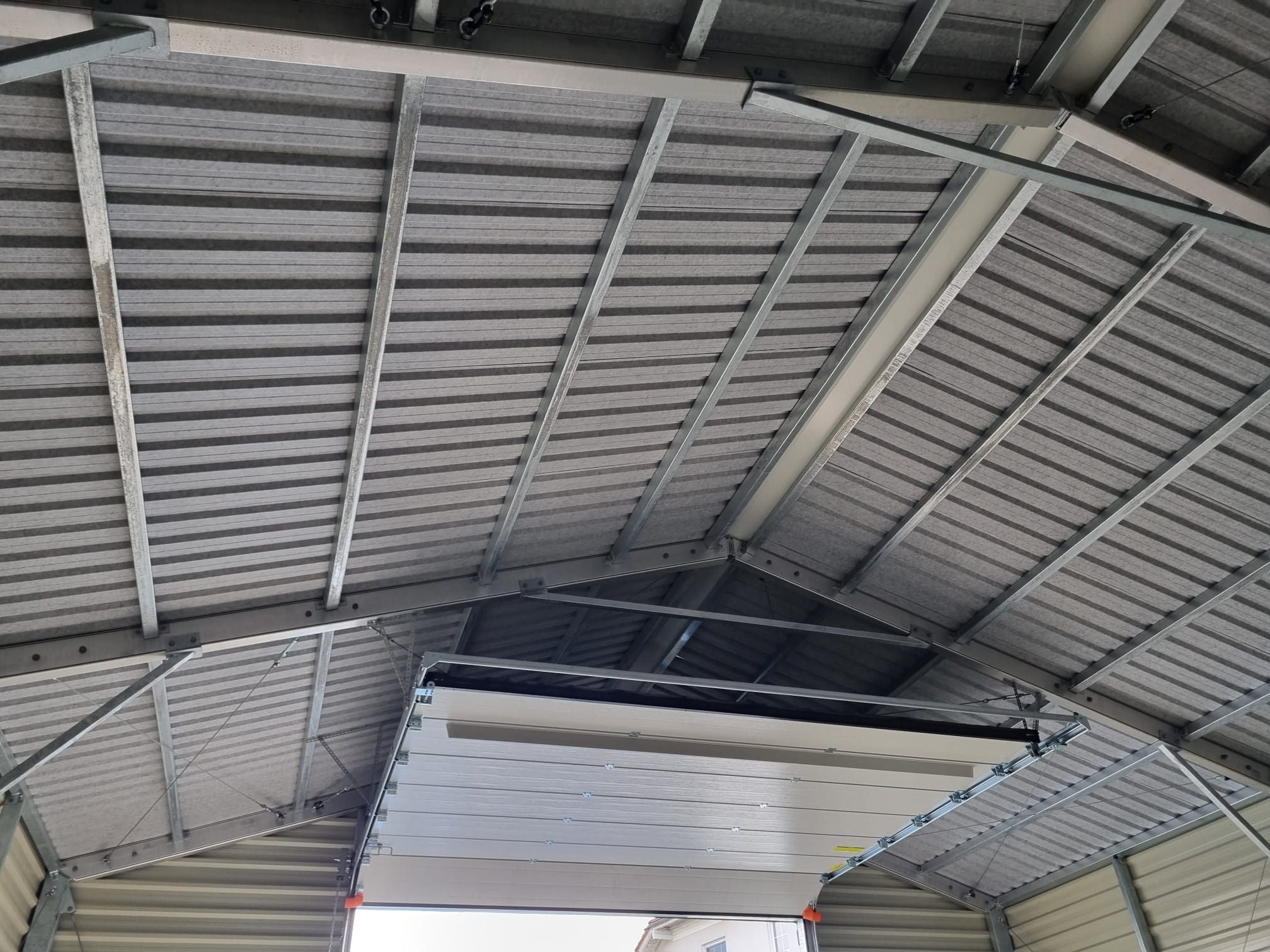 Wnętrze hali z widoczną konstrukcją stalową dachu i częściowo otwartą bramą segmentową.