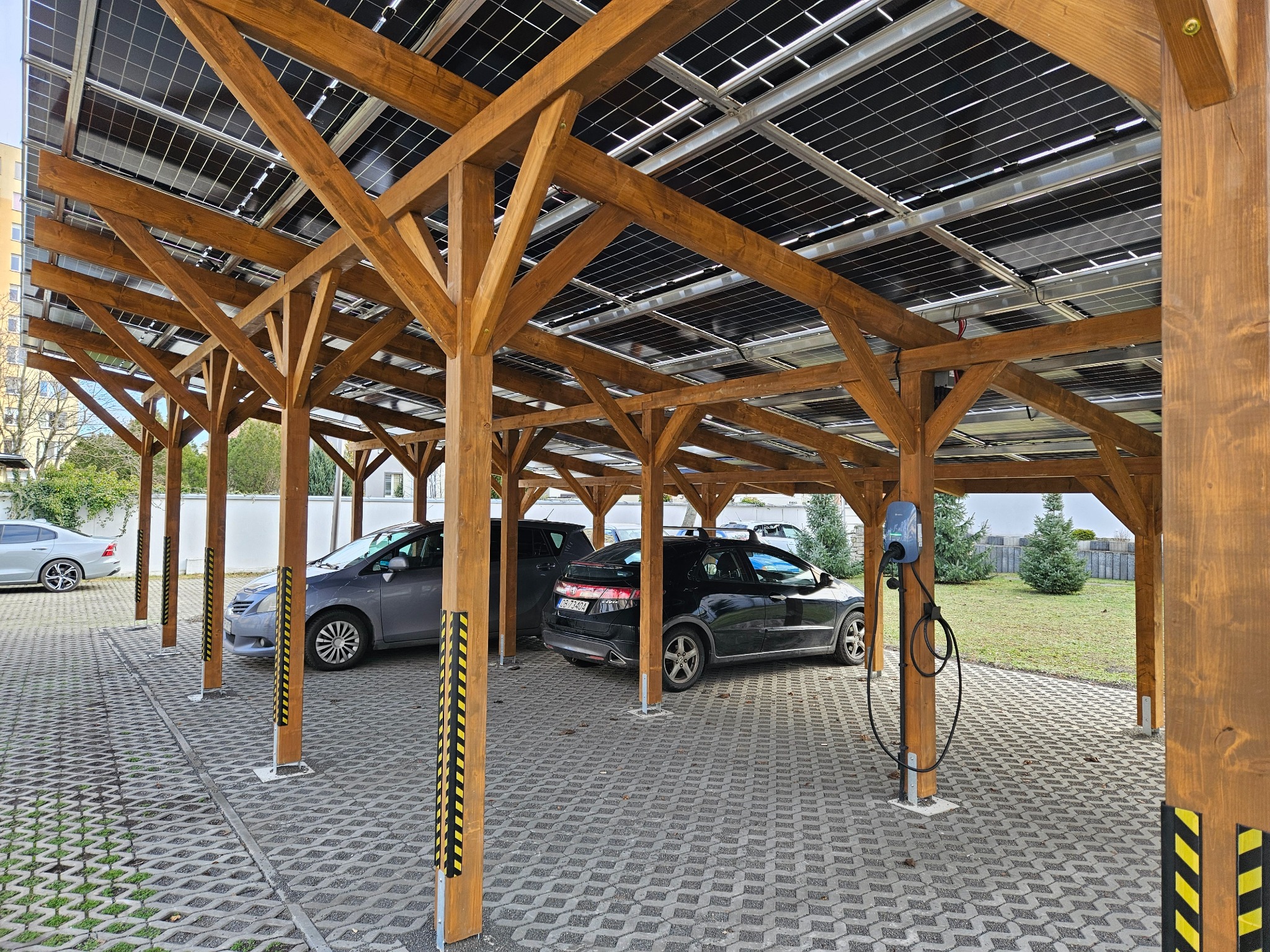 Drewniana wiata parkingowa z panelami fotowoltaicznymi na dachu, stanowisko do ładowania samochodów elektrycznych.