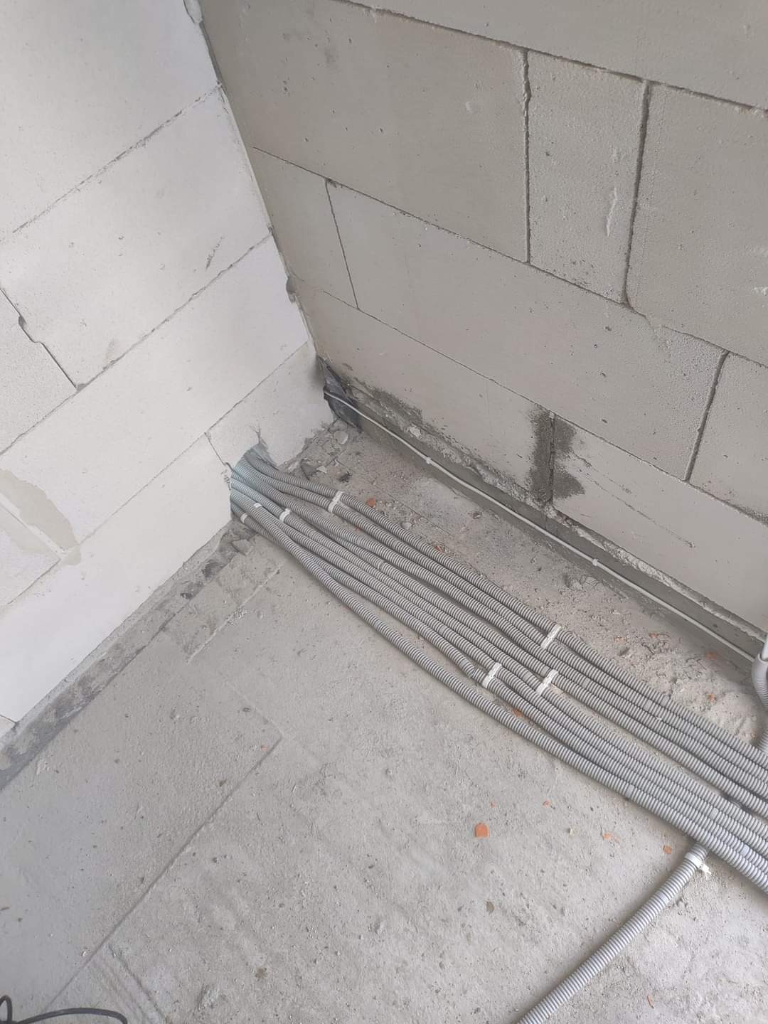 Koryta kablowe ułożone wzdłuż ściany z betonu komórkowego, zabezpieczone białymi opaskami zaciskowymi na surowej podłodze.