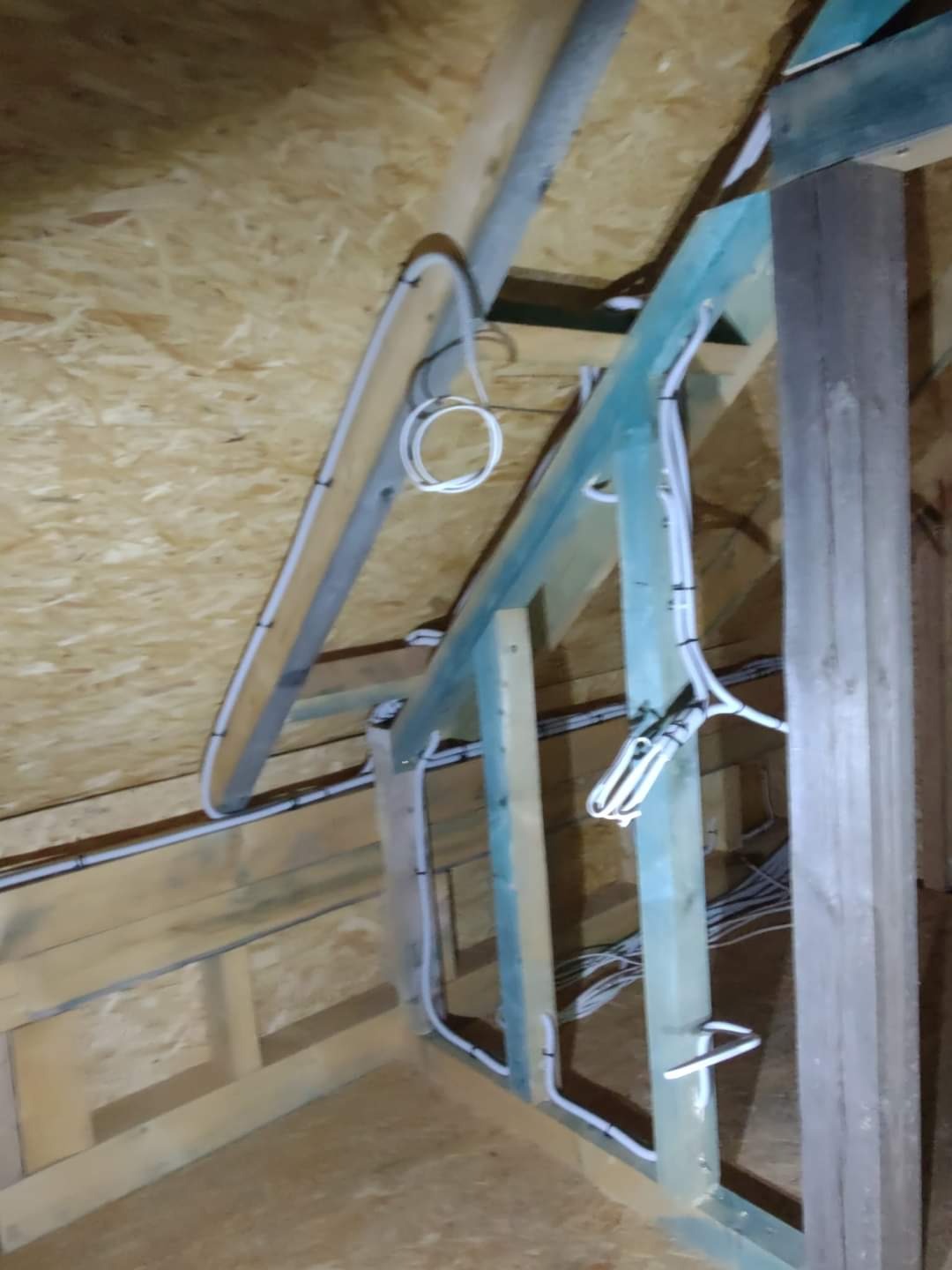 Białe przewody poprowadzone w drewnianej konstrukcji poddasza w Golczewie, widoczne mocowania kabli do belek.