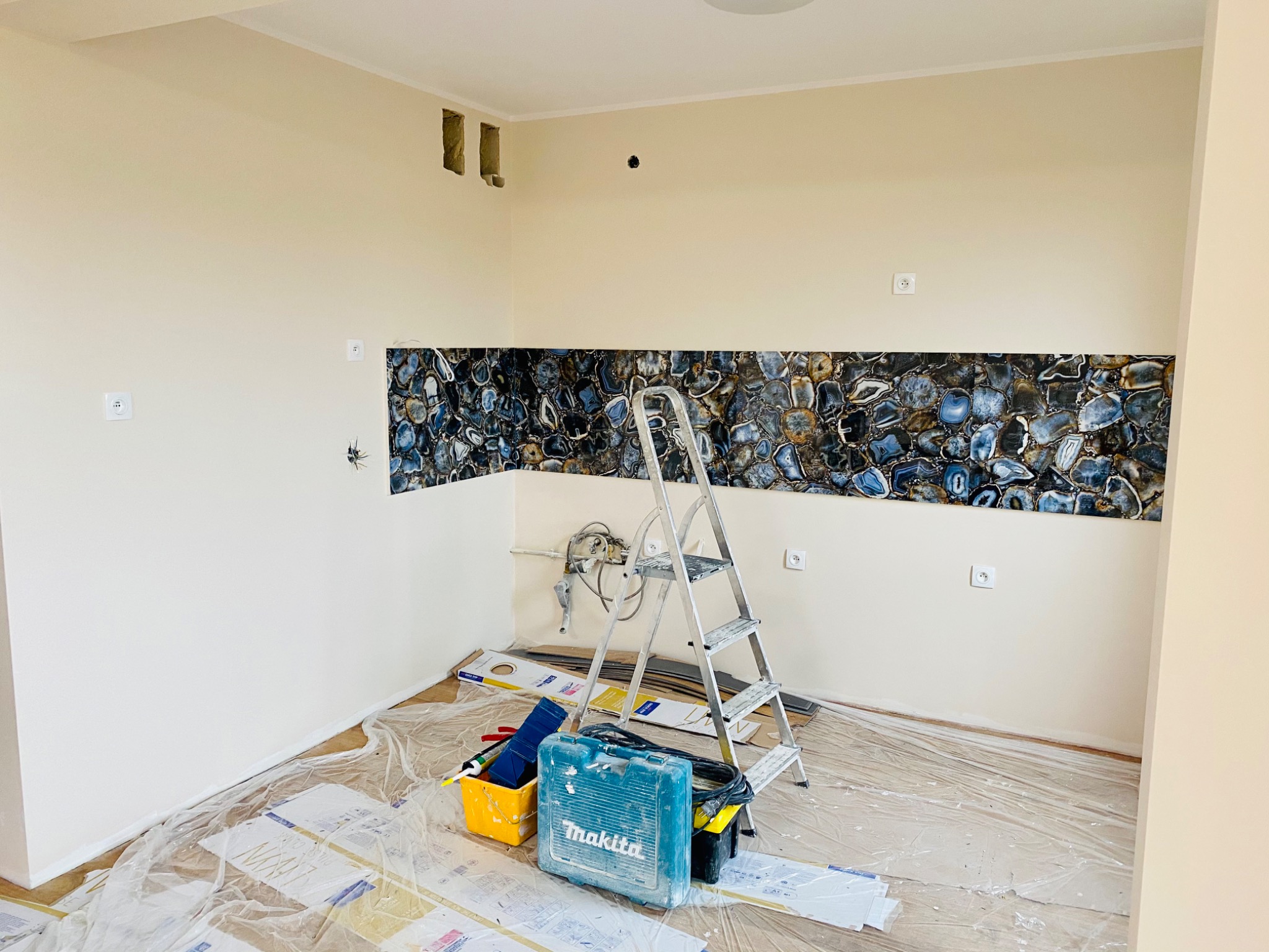 Montaż dekoracyjnego panelu z agatu na ścianie w trakcie remontu, widoczna drabina, narzędzia i zabezpieczona folią podłoga.