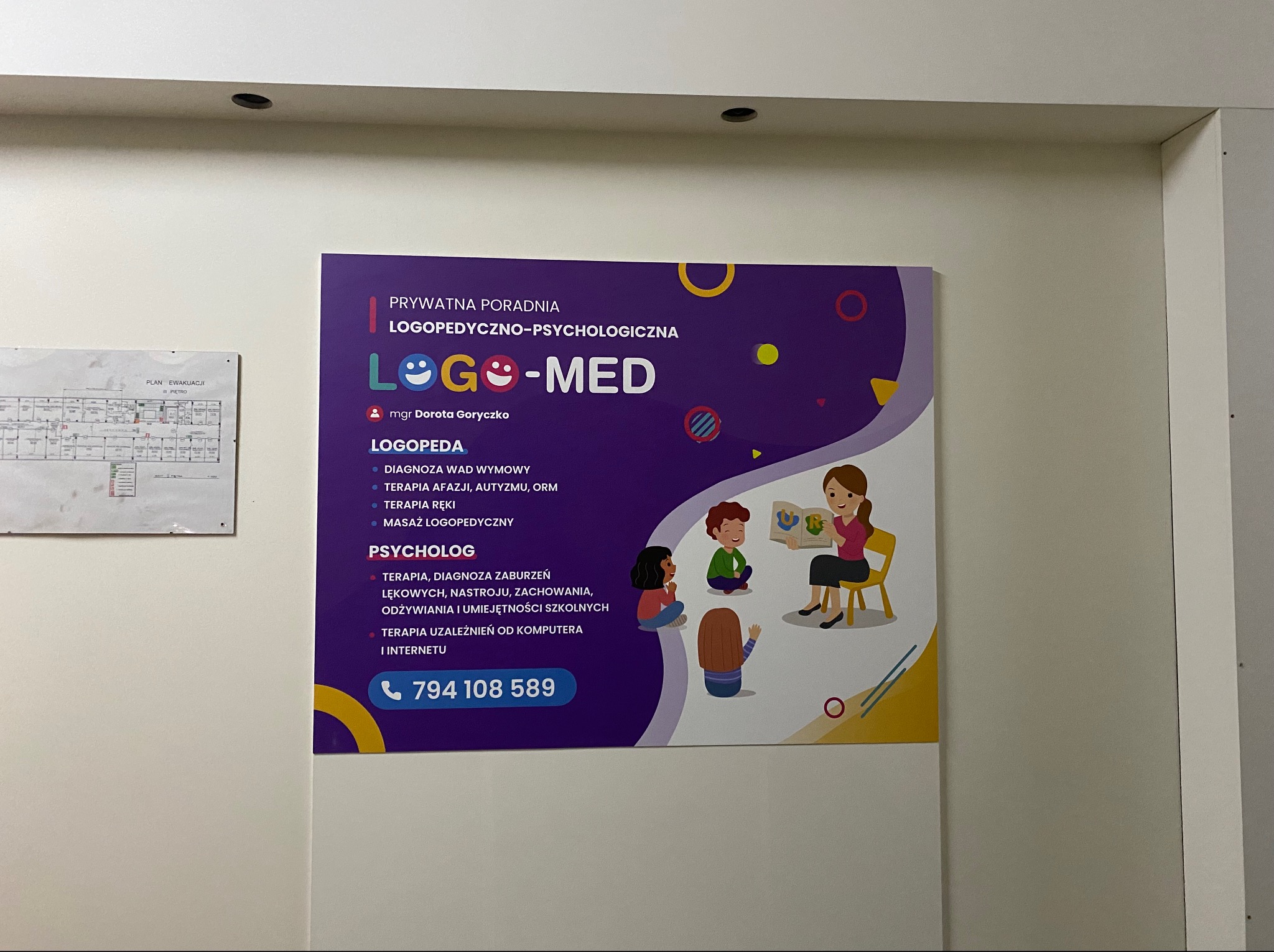 Tablica informacyjna przychodni logopedyczno-psychologicznej z ilustracją terapeuty czytającego książkę grupie dzieci.