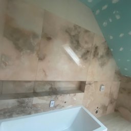 TILER Oleksandr Lebediev - Wnętrze łazienki w trakcie wykańczania: biała wanna, marmurowe płytki, półka w ścianie, sufit z płyt kartonowo-gipsowych przed malowaniem. Widok z góry.