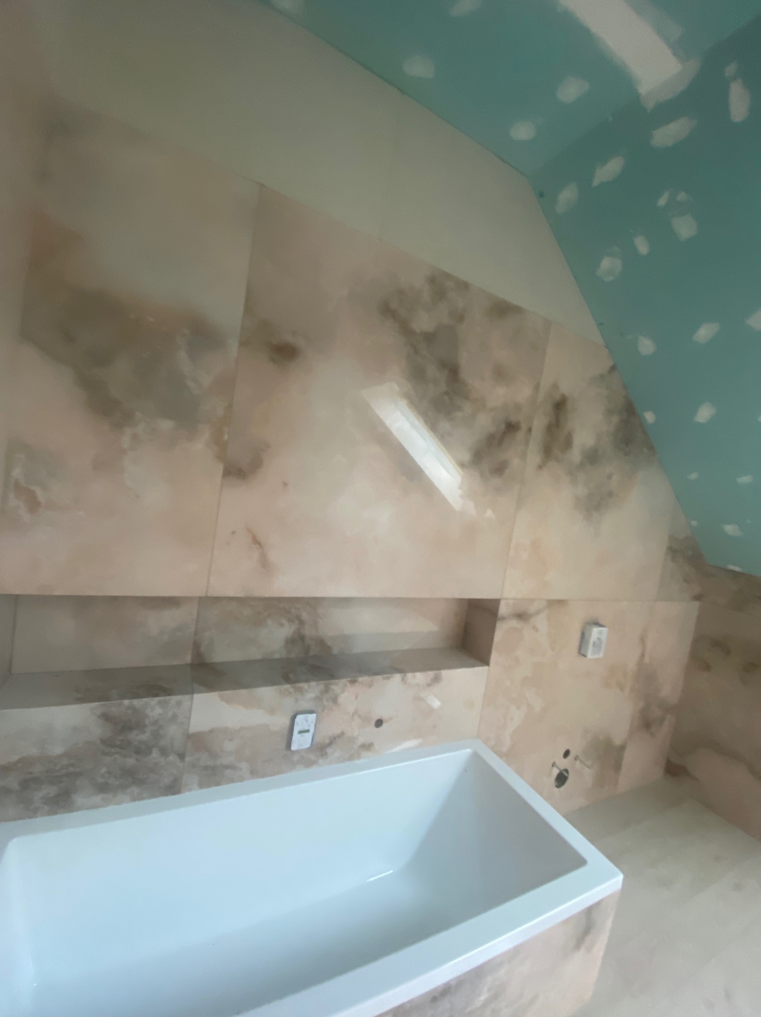 Wnętrze łazienki w trakcie wykańczania: biała wanna, marmurowe płytki, półka w ścianie, sufit z płyt kartonowo-gipsowych przed malowaniem. Widok z góry.