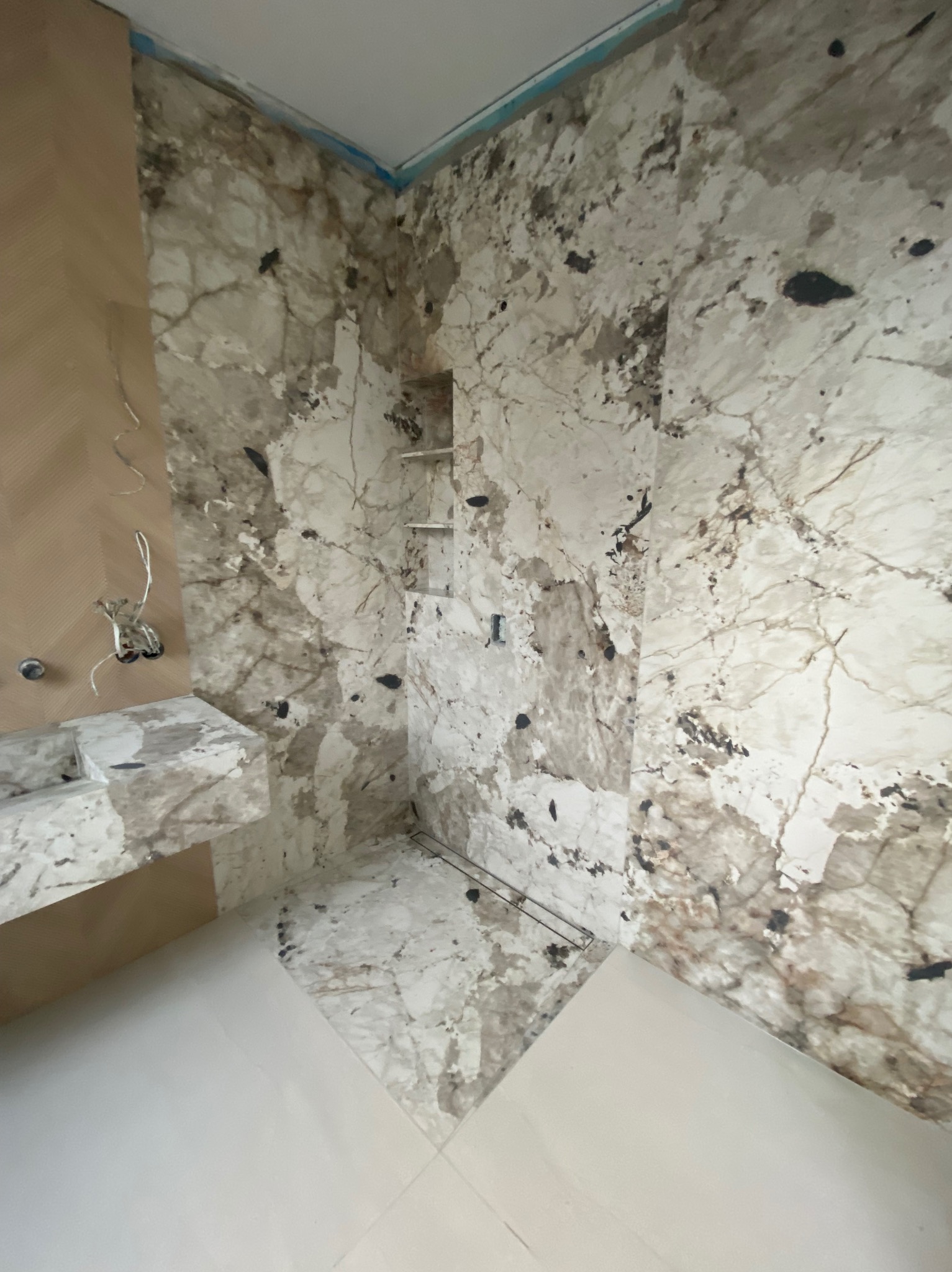 Wykończona łazienka z marmurowymi płytkami na ścianach i podłodze, widoczne elementy armatury i półki wnękowe. Uwagę przykuwa unikalny wzór marmuru.