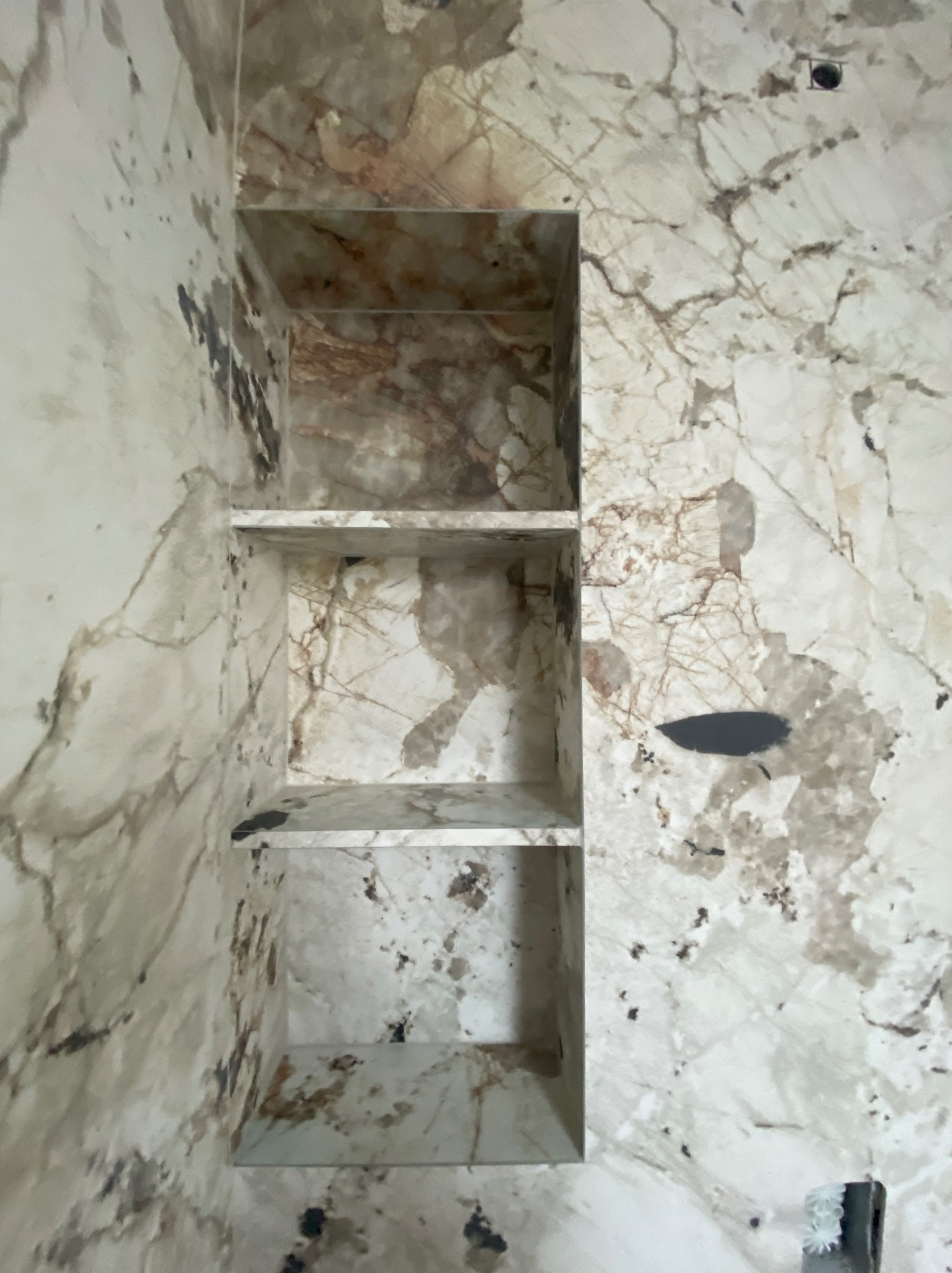 Wykończona wnęka z trzema półkami w łazience, obłożona marmurową płytką w odcieniach bieli i beżu, z widocznymi żyłami. Nowoczesny design.