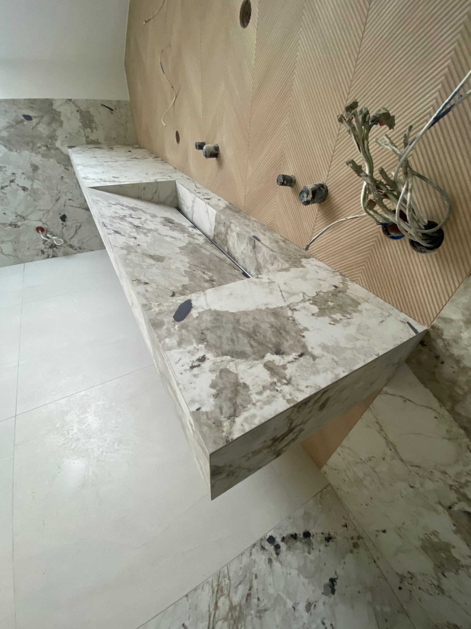 Łazienka w trakcie wykończenia: marmurowa umywalka wpuszczona w blat, wzorzyste płytki na ścianie, widoczne przewody instalacji elektrycznej i hydraulicznej.