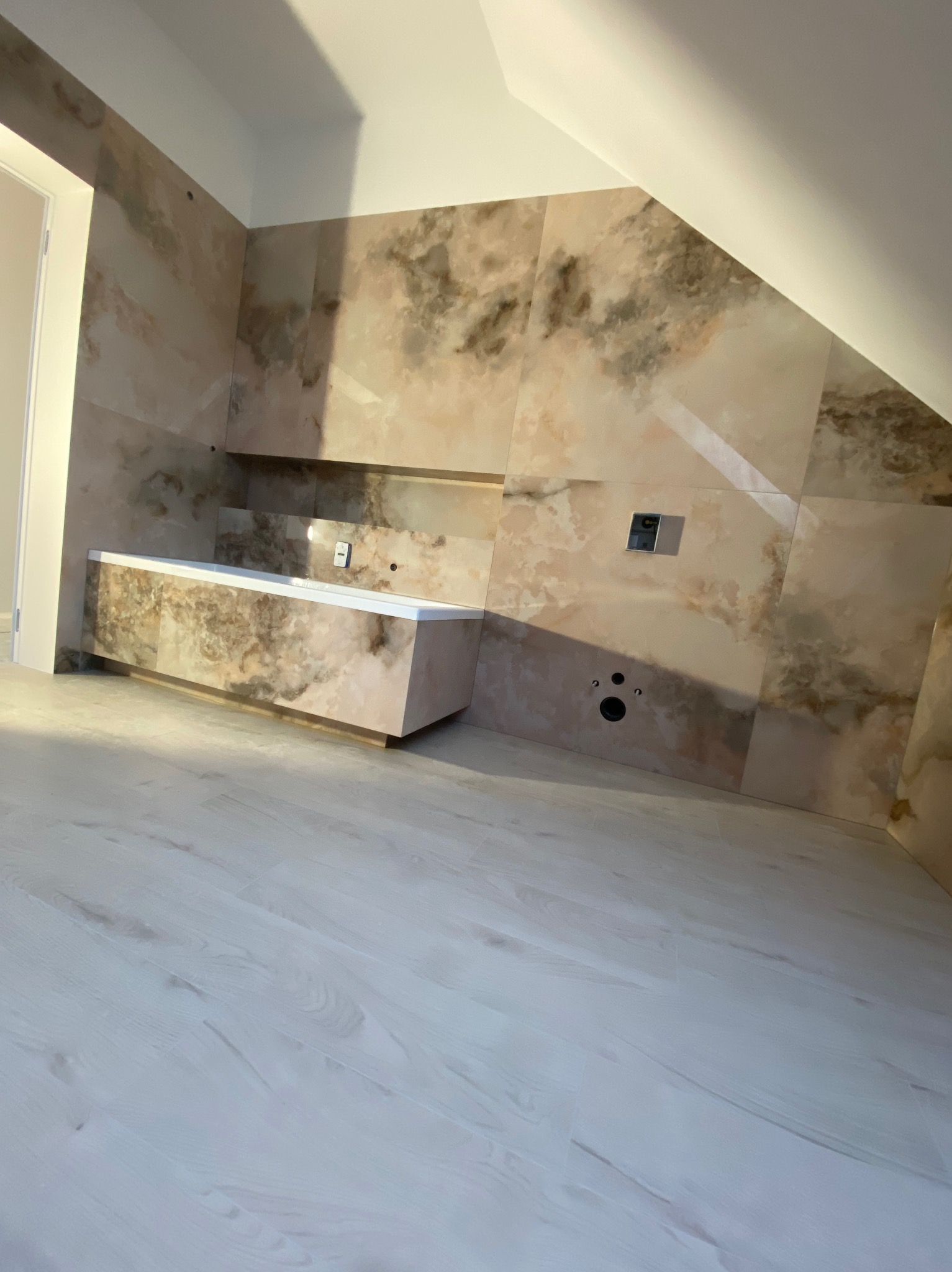 Wykończona łazienka na poddaszu z beżowymi płytkami imitującymi marmur na ścianach i obudowie wanny. Jasne panele podłogowe.