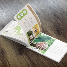 A2 studio - Otwarty katalog reklamowy leżący na drewnianej powierzchni, prezentujący wizualizacje osiedla mieszkaniowego z hasłami o zdrowym stylu życia.