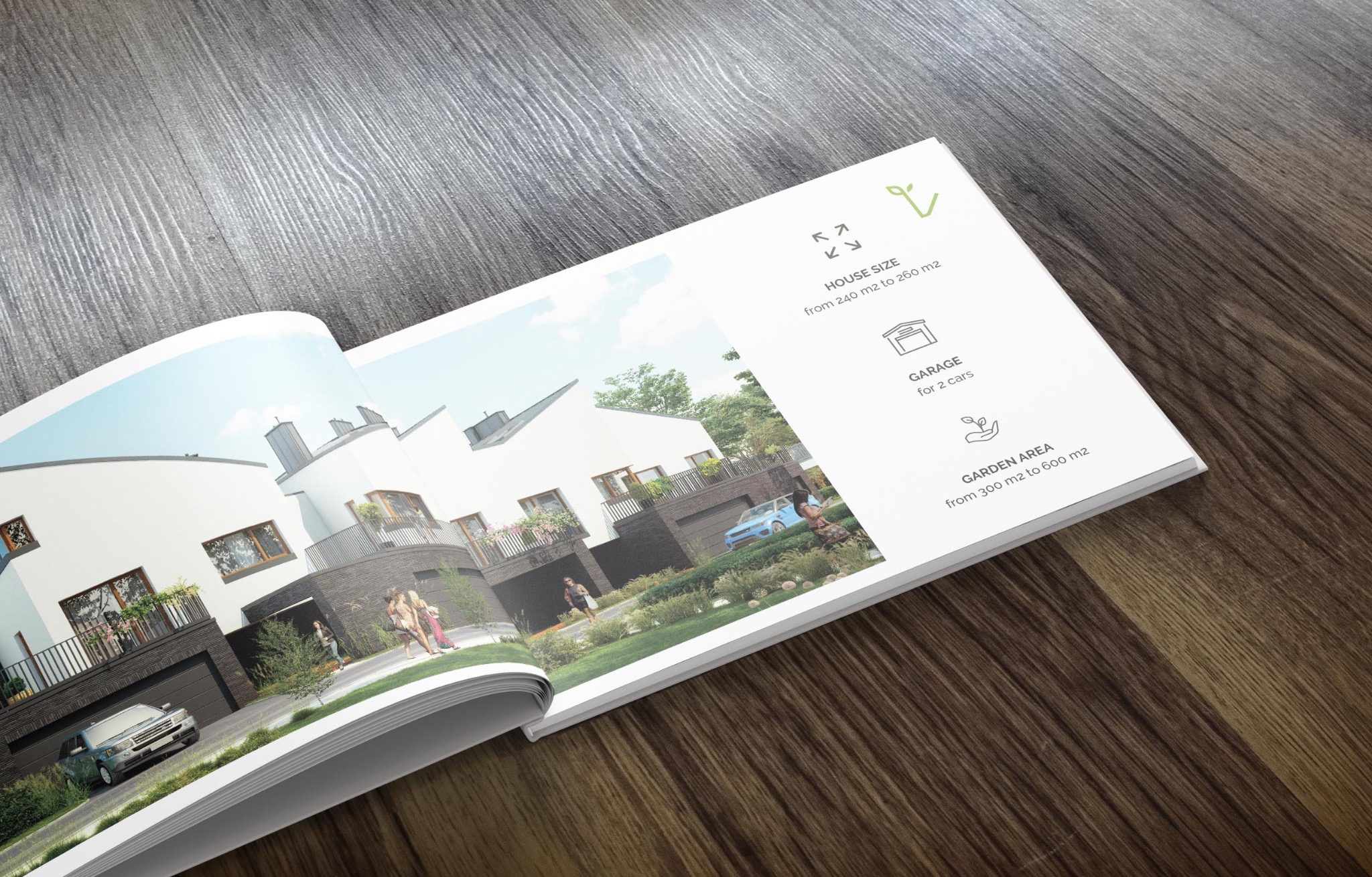 Otwarta broszura reklamowa leżąca na drewnianym stole prezentuje wizualizację osiedla domów jednorodzinnych z samochodami i zadbaną zielenią, zawierająca informacje o powierzchni domów, garaży...