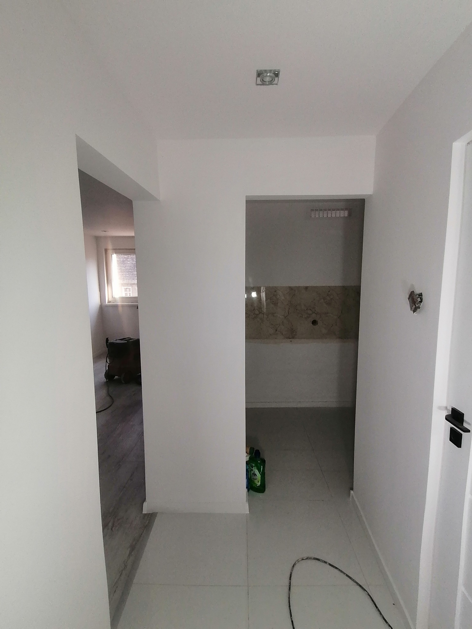 Wnętrze mieszkania po remoncie: białe ściany, jasna podłoga, widoczne przejścia do innych pomieszczeń, butelki z środkami czyszczącymi w rogu.