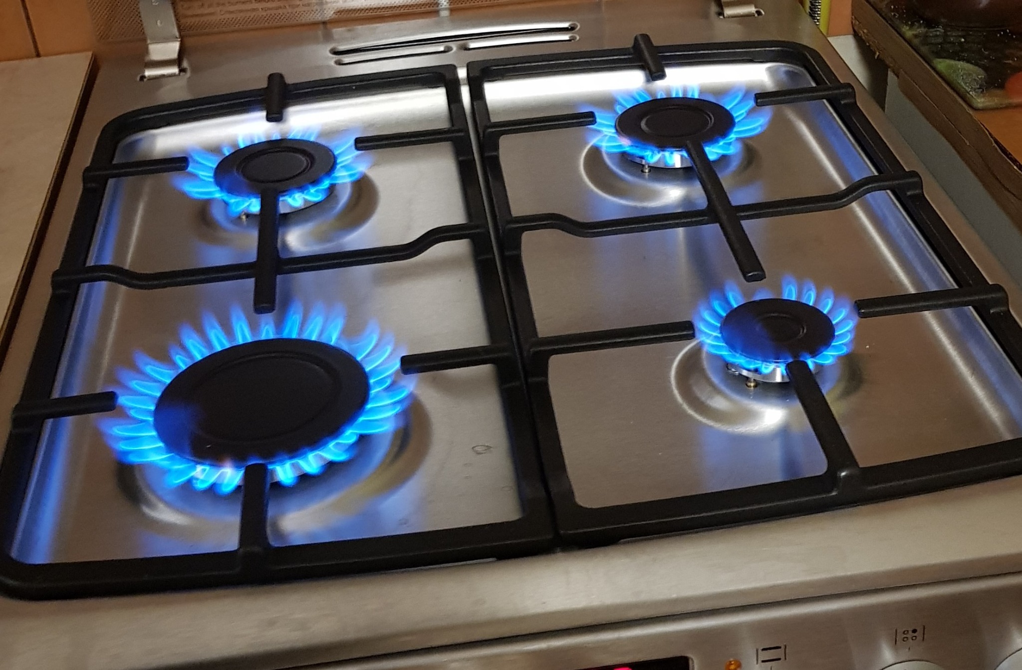 Cztery palniki gazowe z intensywnym niebieskim płomieniem na nowoczesnej, srebrnej płycie kuchennej.