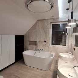 Grzegorz Szymoniak - Nowoczesna łazienka na poddaszu z wolnostojącą wanną, dwiema okrągłymi umywalkami nablatowymi, marmurowymi płytkami na ścianach i drewnopodobną podłogą; widoczna zabudowa meblowa z białymi frontami...