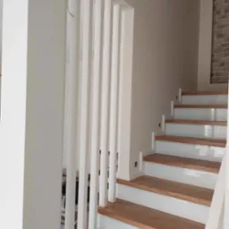 Nowoczesne schody z drewnianymi stopniami i białymi podstopnicami, z pionowymi białymi elementami balustrady, widok z dołu.